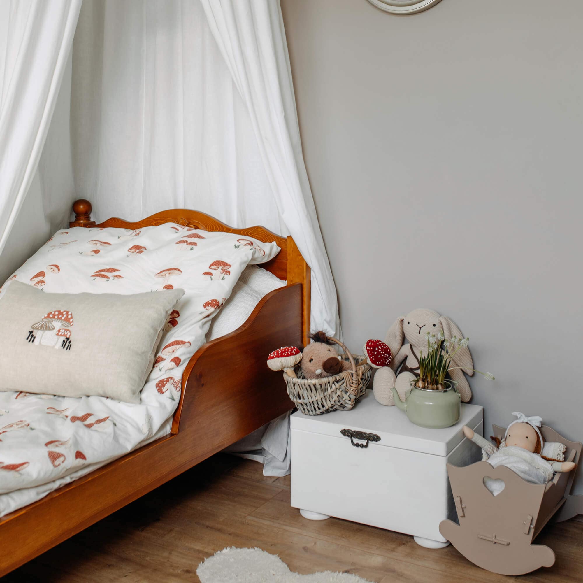 Houten kinderbed met wit beddengoed met paddenstoelenprint en knuffels op witte kist