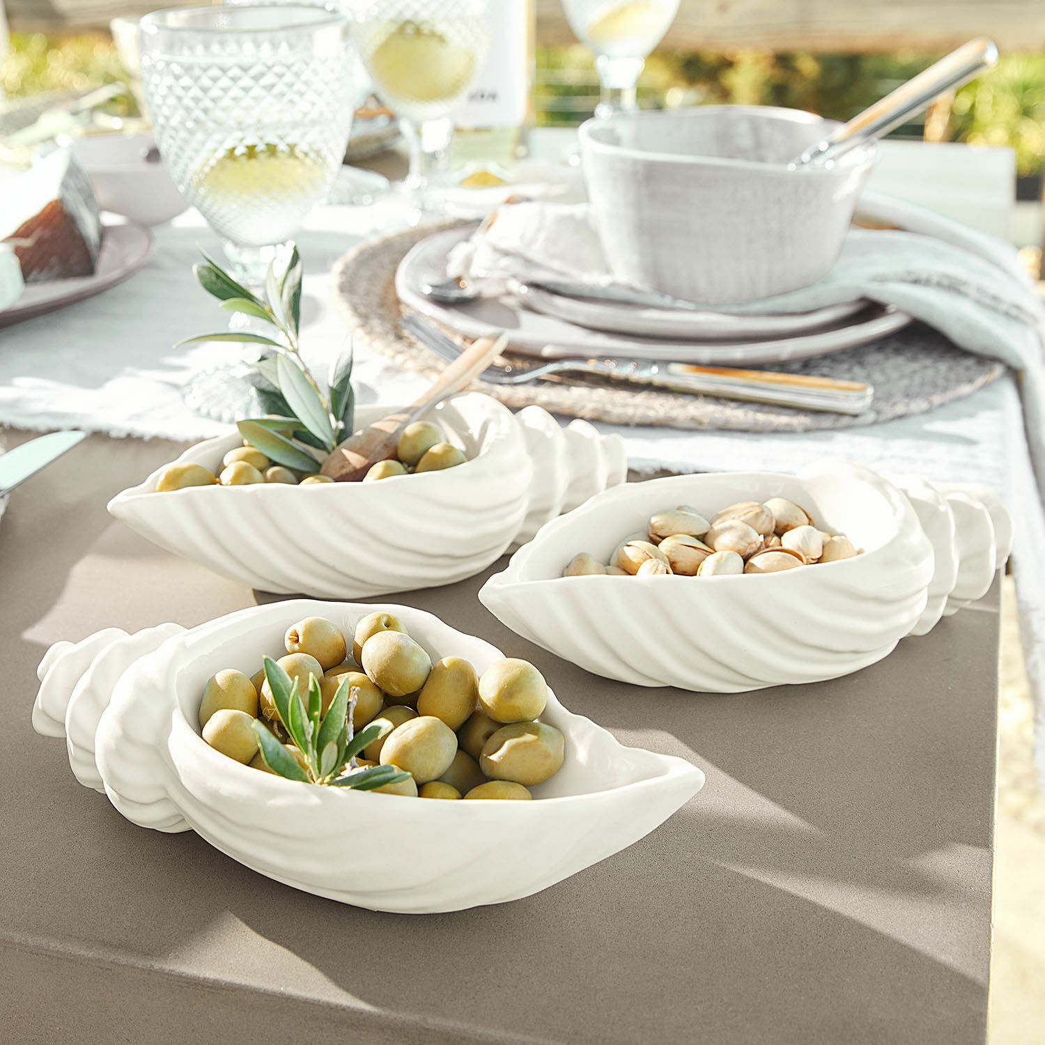 Witte keramische schaaltjes in schelpvorm met olijven en noten op tuintafel