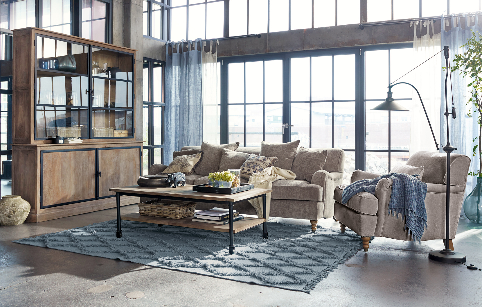 Gezellige loft woonkamer met beige bank, houten kast en blauw vloerkleed op betonnen vloer