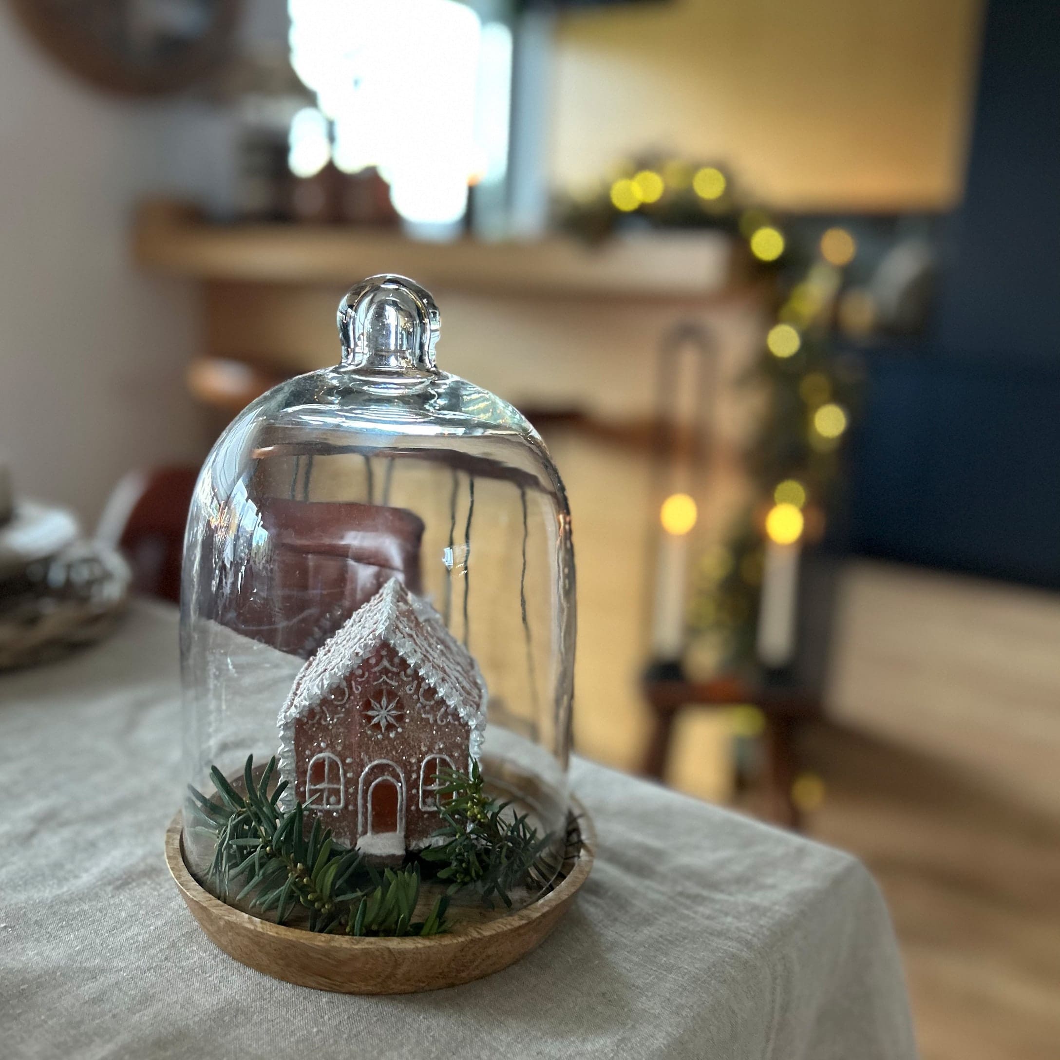 Decoratief peperkoekhuisje onder glazen stolp op houten schaal met groene takken