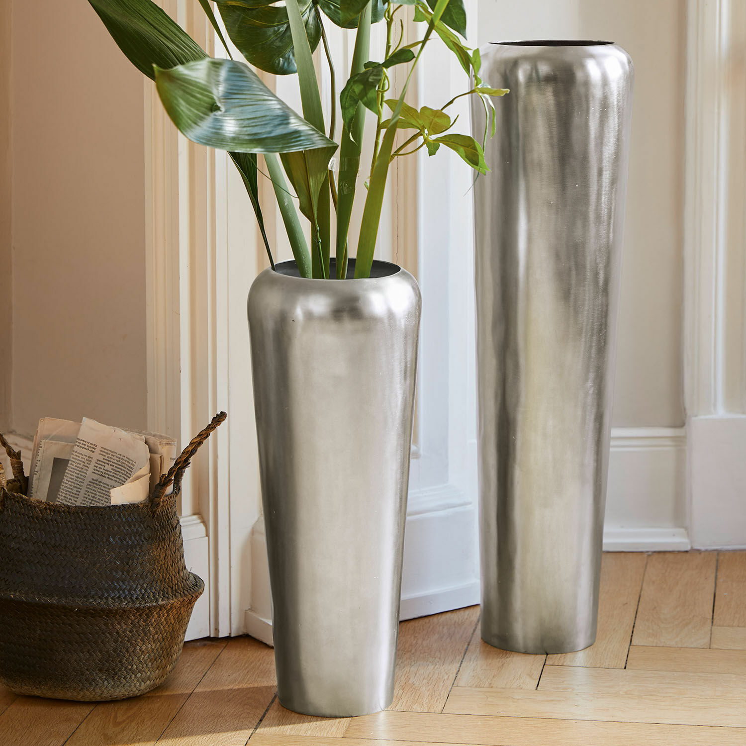 Vloervaas set van 2 Carolan Twee hoge zilveren metalen vazen op de vloer in een lichte kamer met groene planten