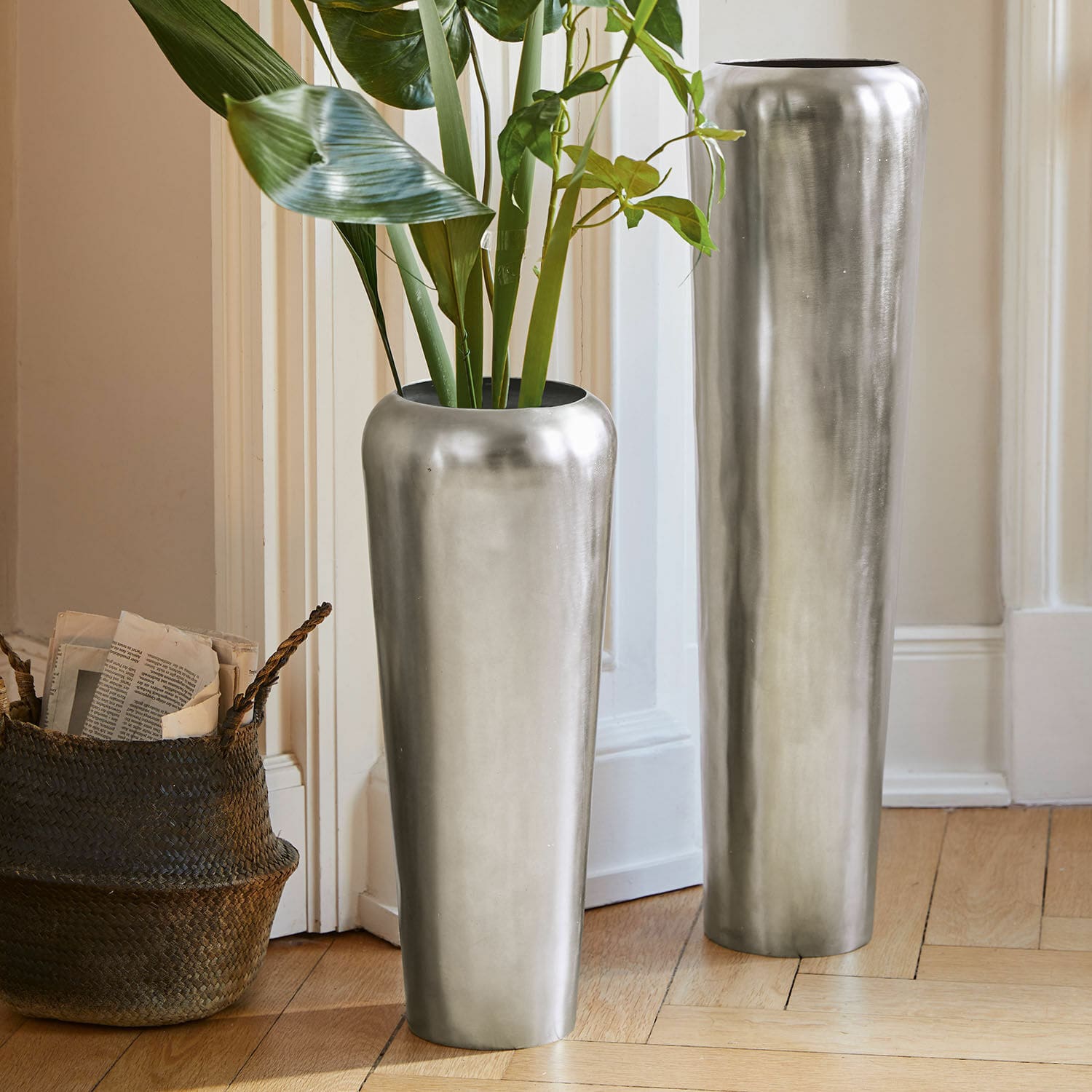 Vloervaas set van 2 Carolan Twee hoge zilveren metalen vazen op de vloer in een lichte kamer met groene planten