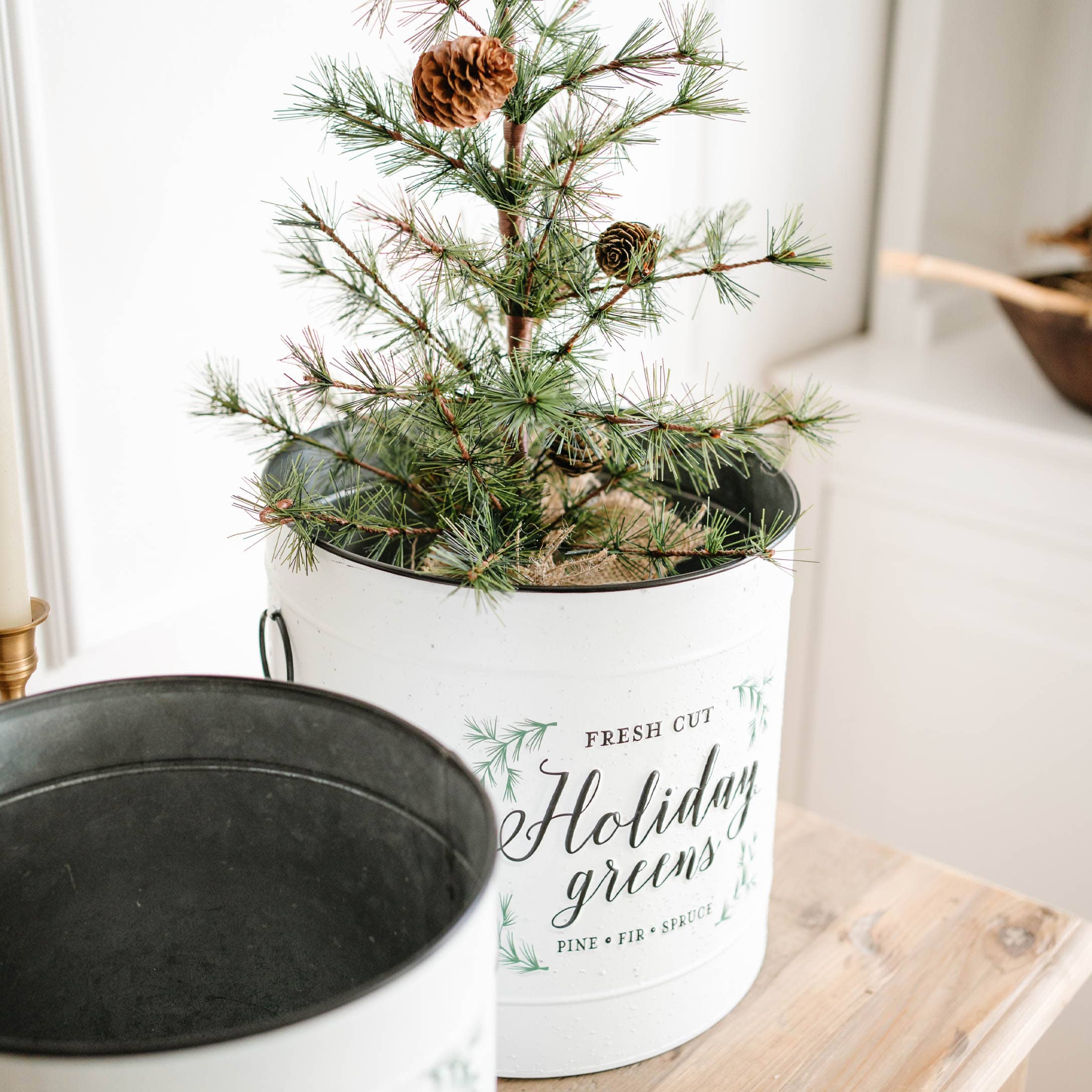 Witte metalen pot met groene dennen takken en dennenappels op houten tafel