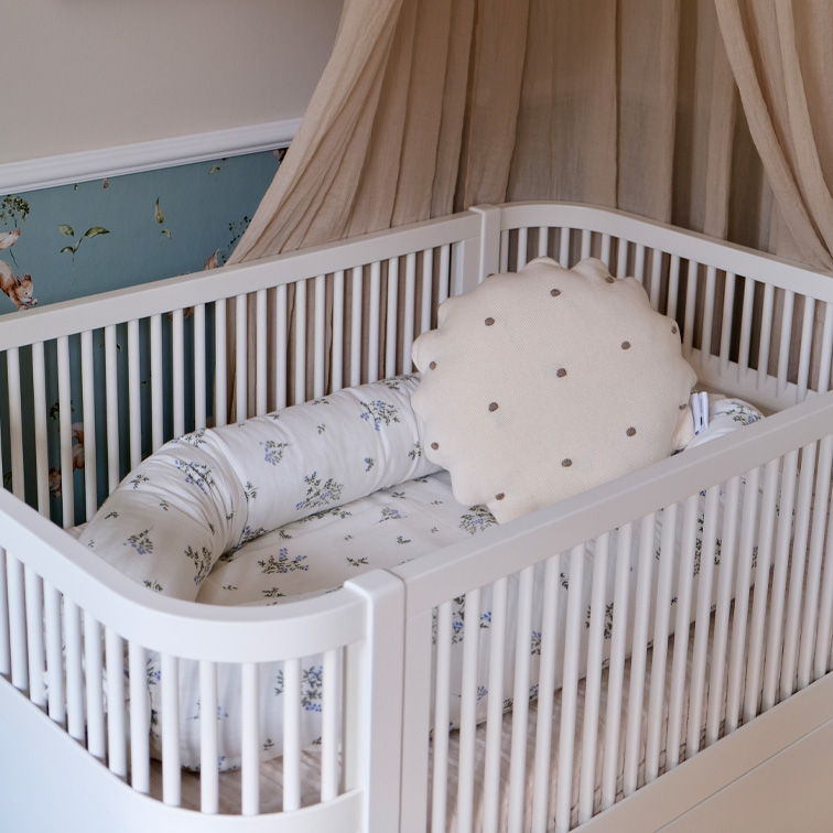 Witte babybed met zacht kussen en beddengoed met bloemenpatroon in pasteltinten