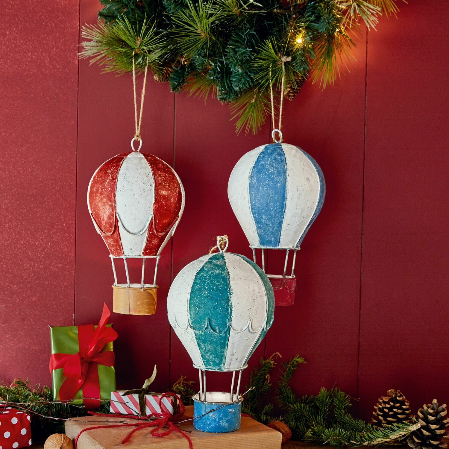 Metalen luchtballonversieringen tegen een rode muur met groene takken en cadeaus