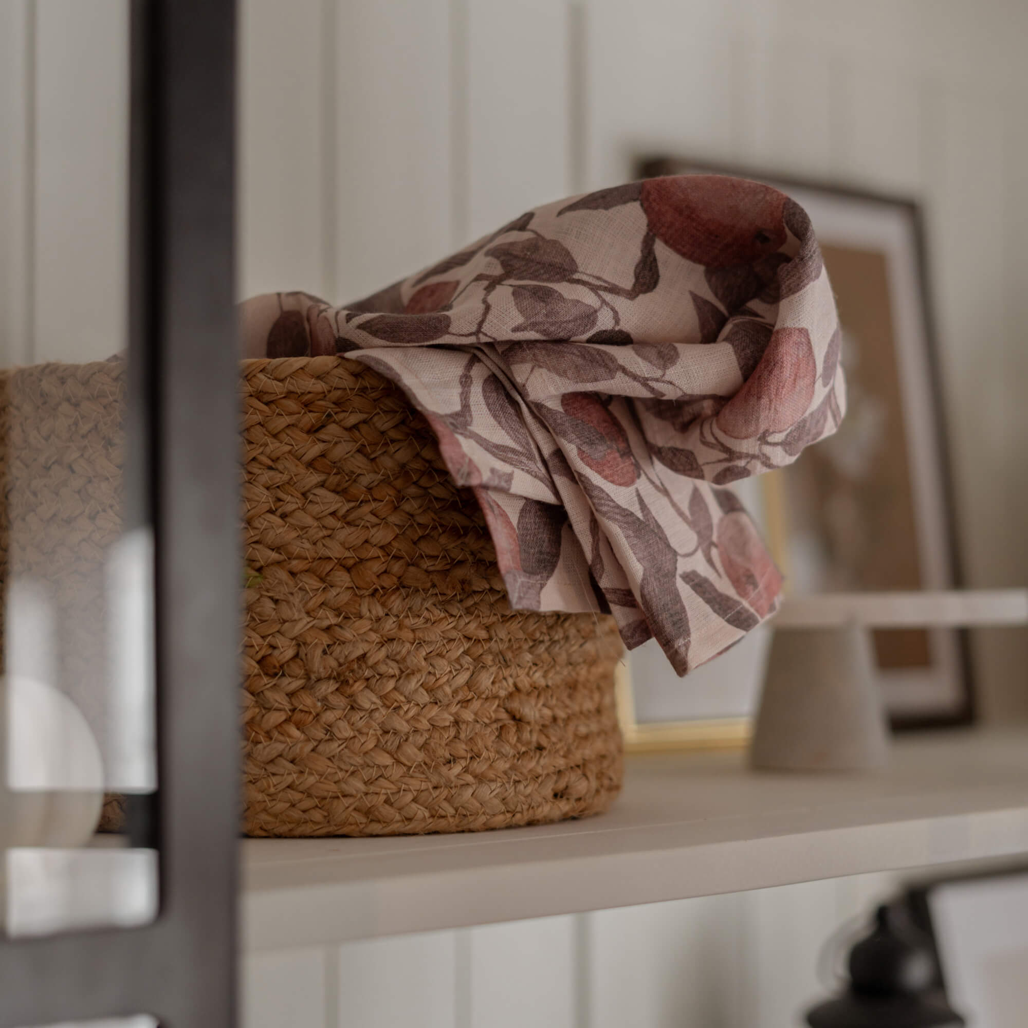 Mand van natuurlijk gevlochten materiaal met linnen stof in roze-bruine bloemenprint op witte plank