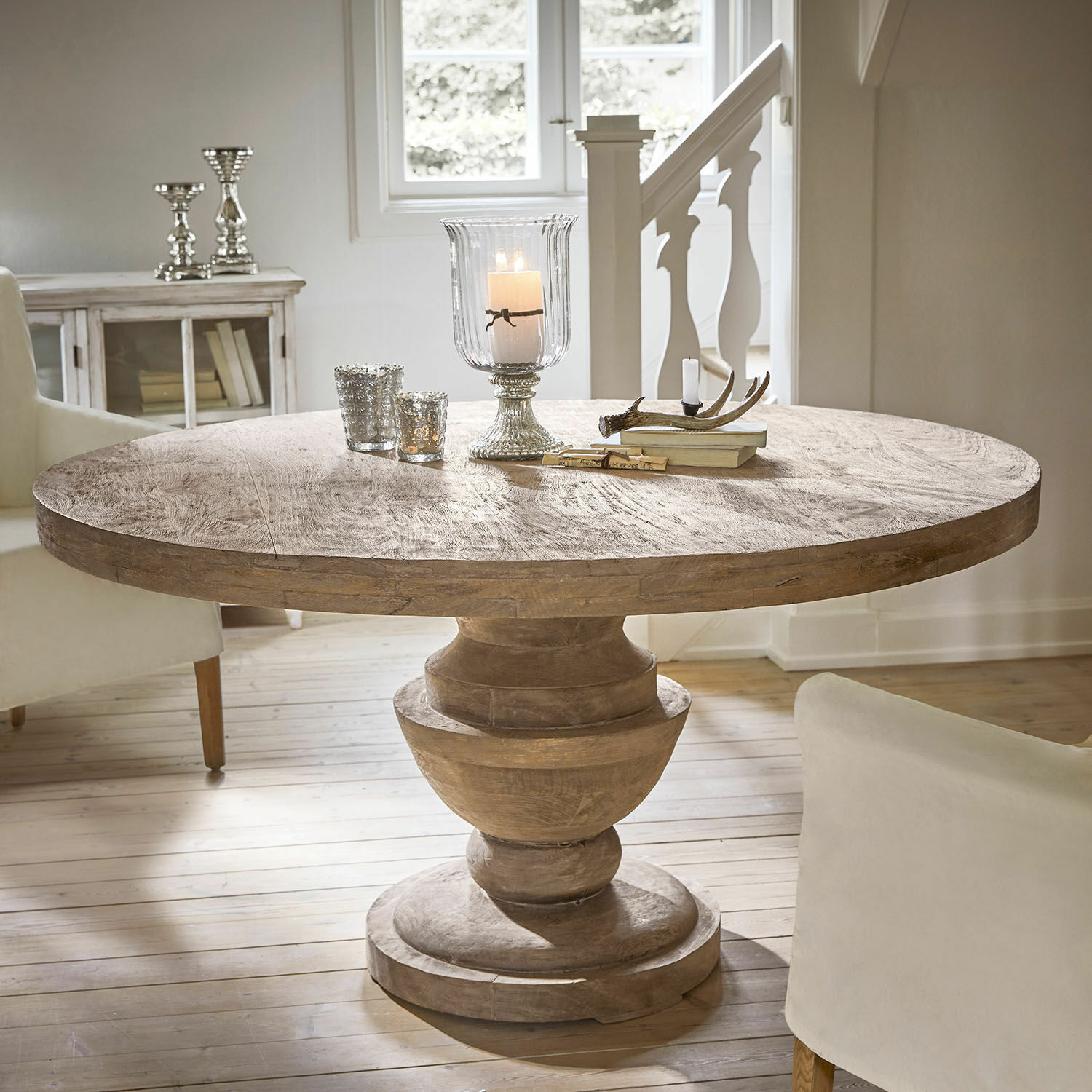 Ronde mangohouten tafel in natuurlijke kleur met decoratieve kandelaars en boeken erop in lichte kamer