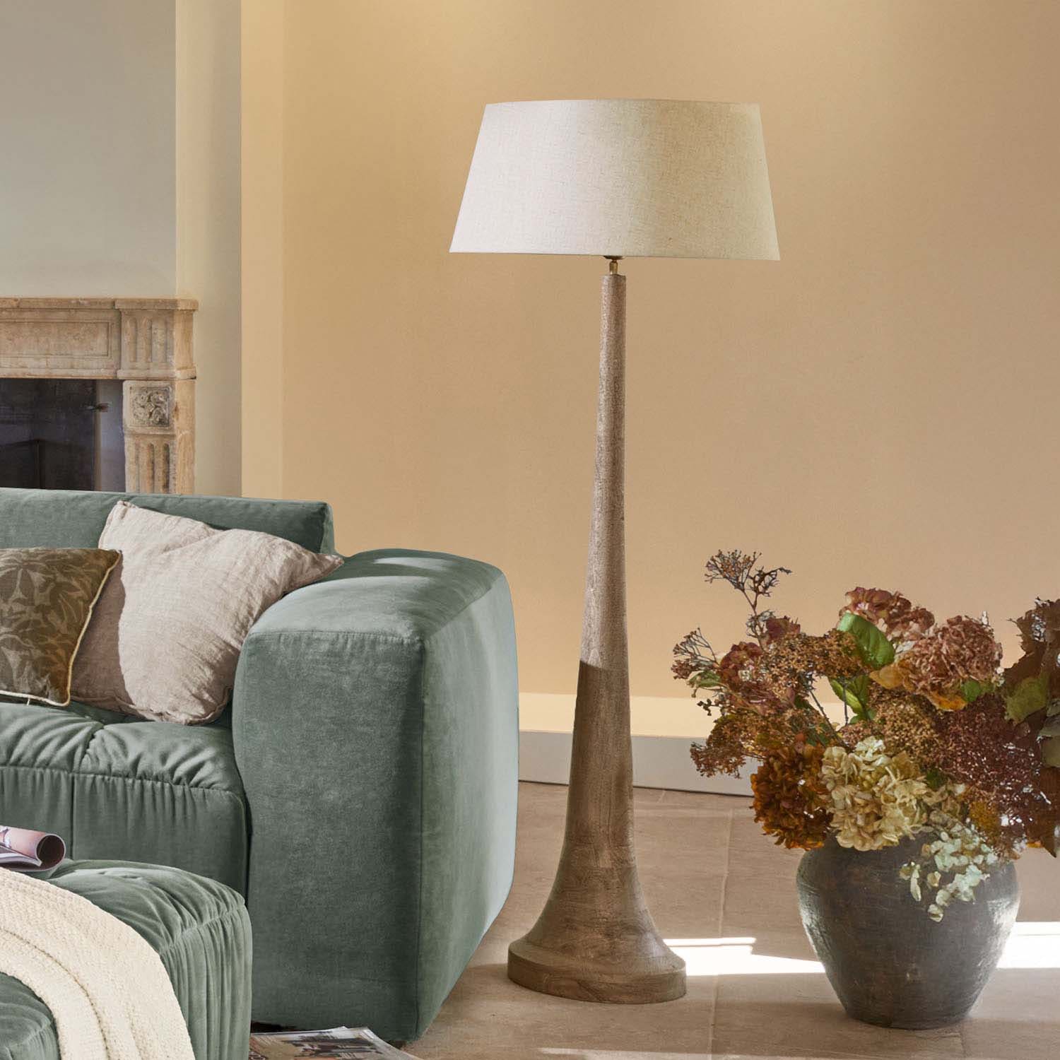 Vloerlamp met houten voet en beige kap in moderne woonkamer met groene bank en droogbloemen