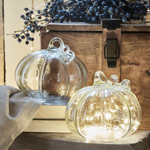 Decoratieve glazen pompoenen in doorzichtig glas met zachte LED-verlichting tegen een rustieke houten achtergrond