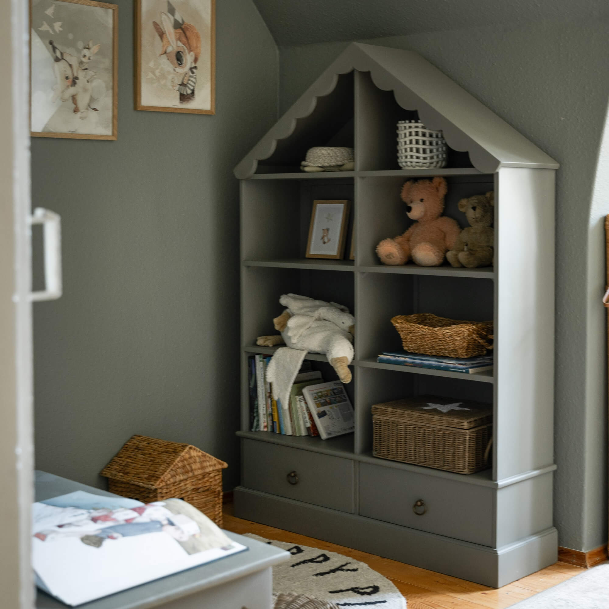 Grijze houten kast in huisvorm met knuffels en opbergmanden in kinderkamer