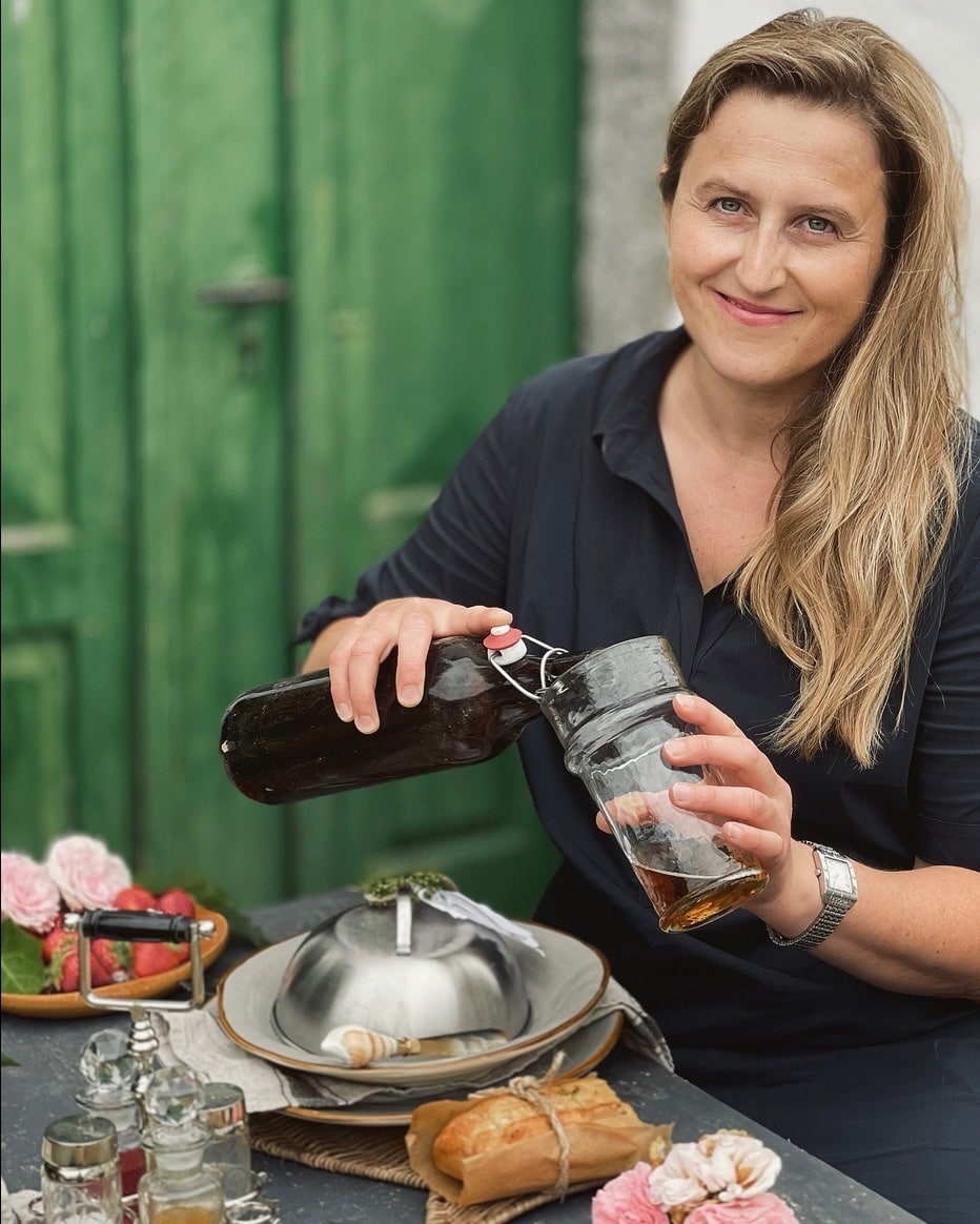 Vrouw schenkt drank uit glazen fles in glas aan tafel met eten en bloemen