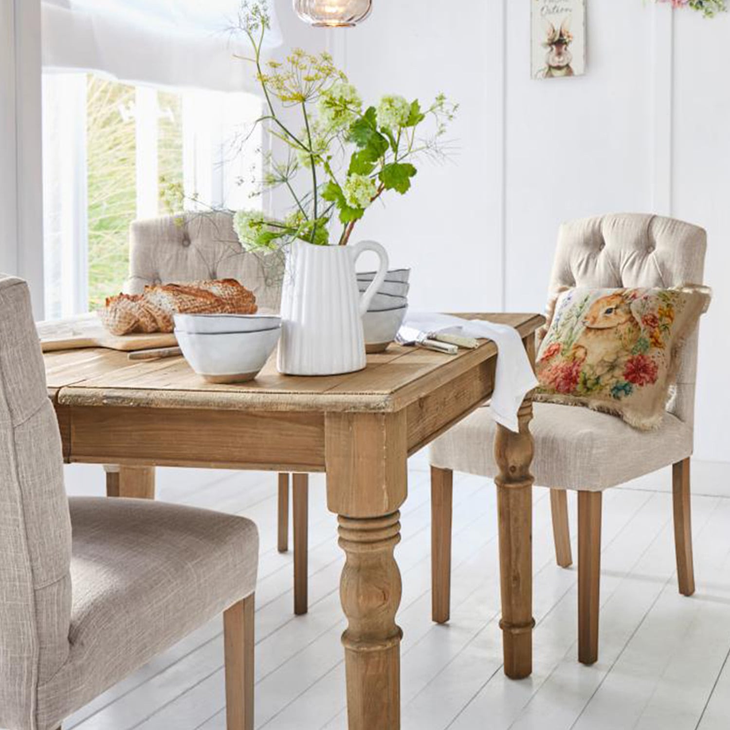 Lichte houten tafel met decoratieve kan en kommen, beige gestoffeerde stoelen in lichte eetkamer