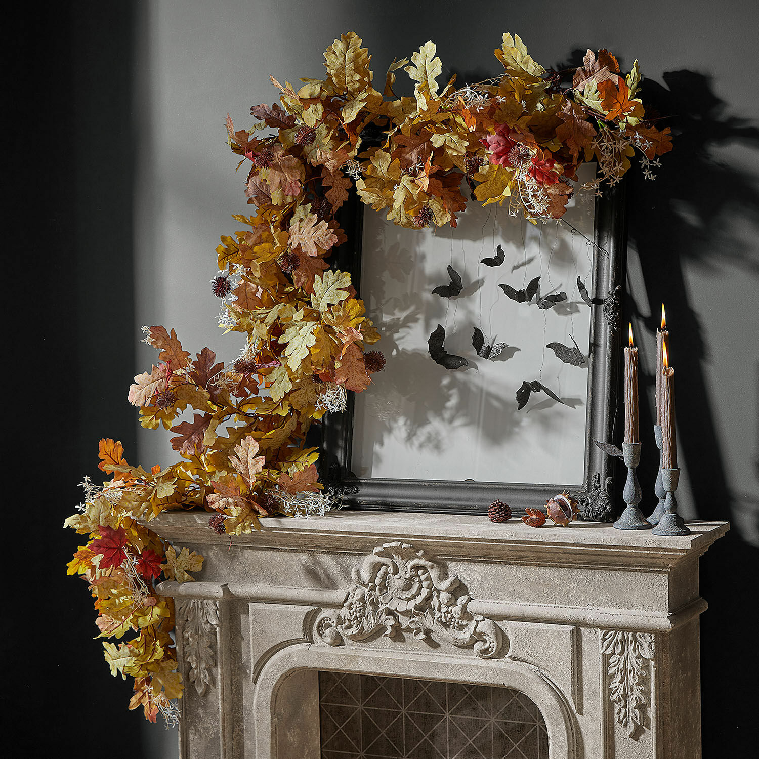 Guirlande Fleurimont Decoratieve herfstkrans van eikenbladeren in warme tinten op stenen open haard met zwarte lijst en kaarsen