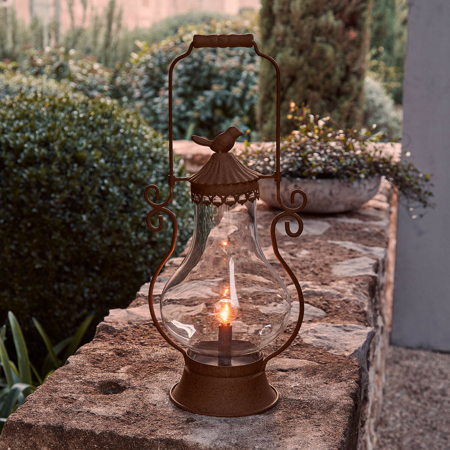 Tuinlantaarn van roestig metaal met helder glas en vogelornament, geschikt voor terras en tuin
