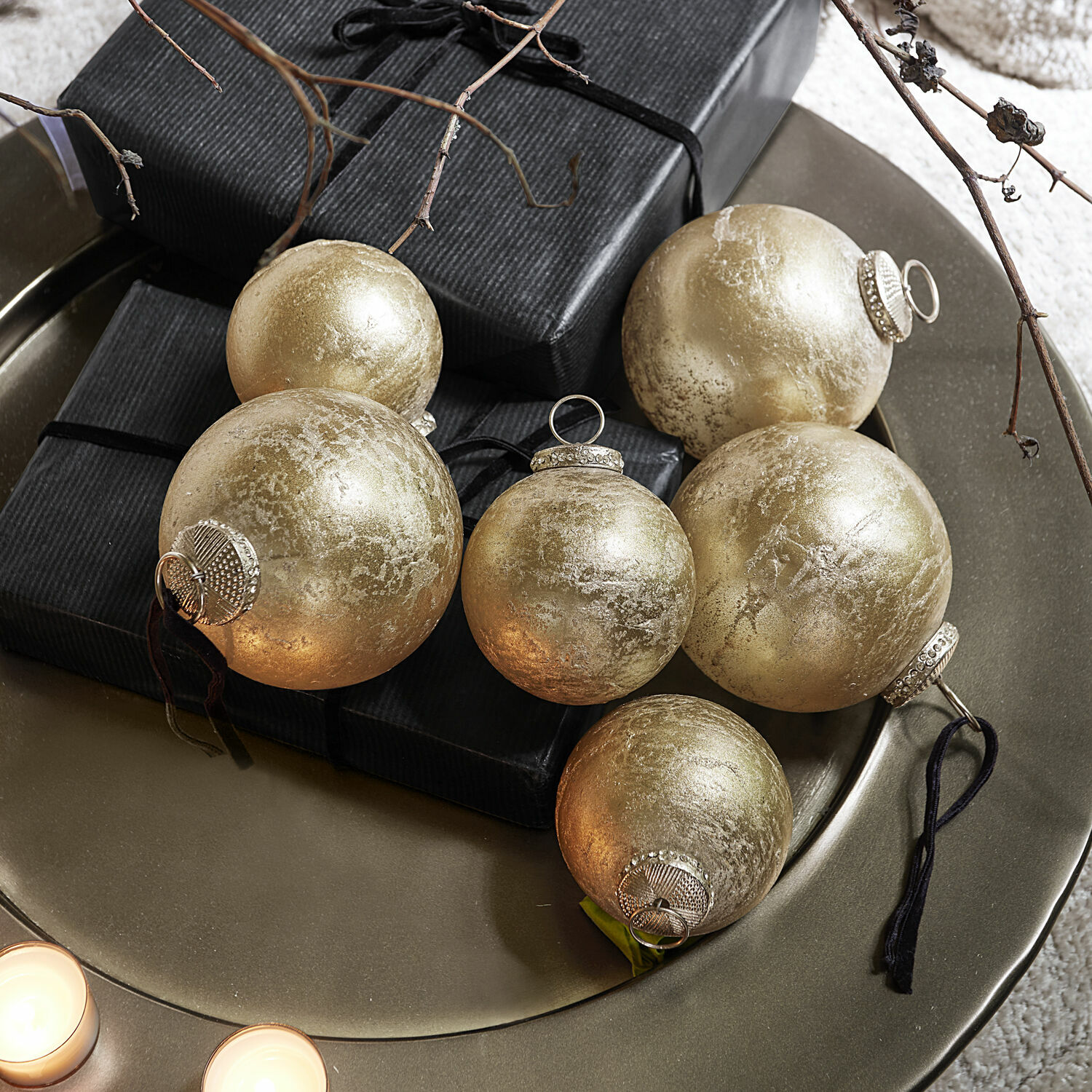 Set gouden glazen kerstballen op metalen schaal met zwarte cadeaus en kaarsen