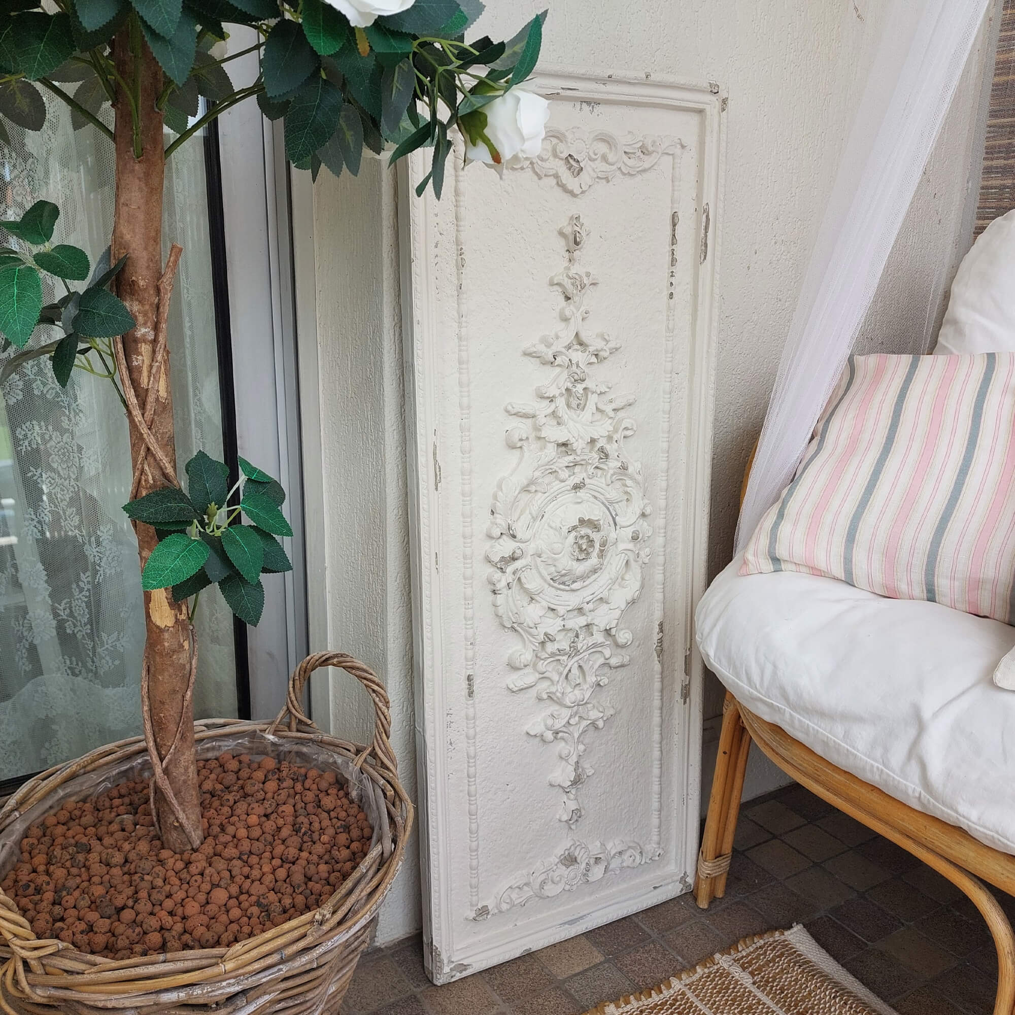 Wit decoratief wandpaneel met vintage ornament naast een rieten mand met plant