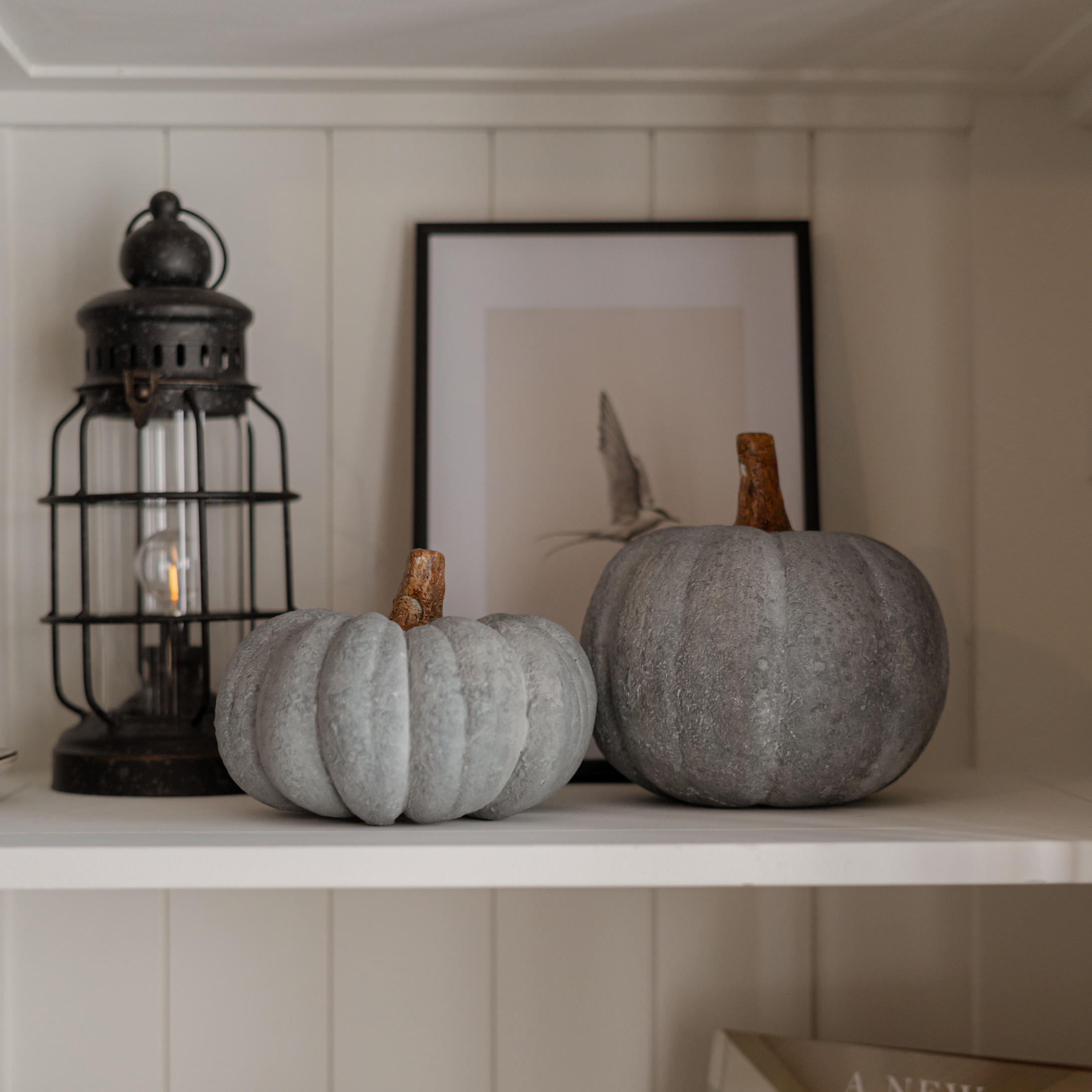 Twee grijze decoratieve pompoenen van steenachtig materiaal op een witte landelijke plank