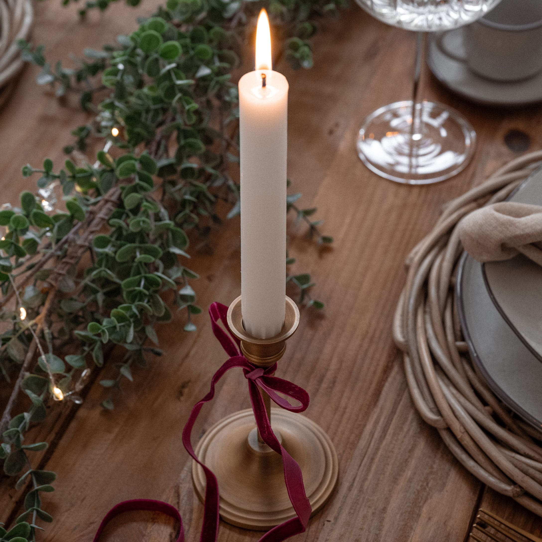 Gouden metalen kandelaar met witte kaars en bordeaux lint op houten tafel met kerstdecoratie