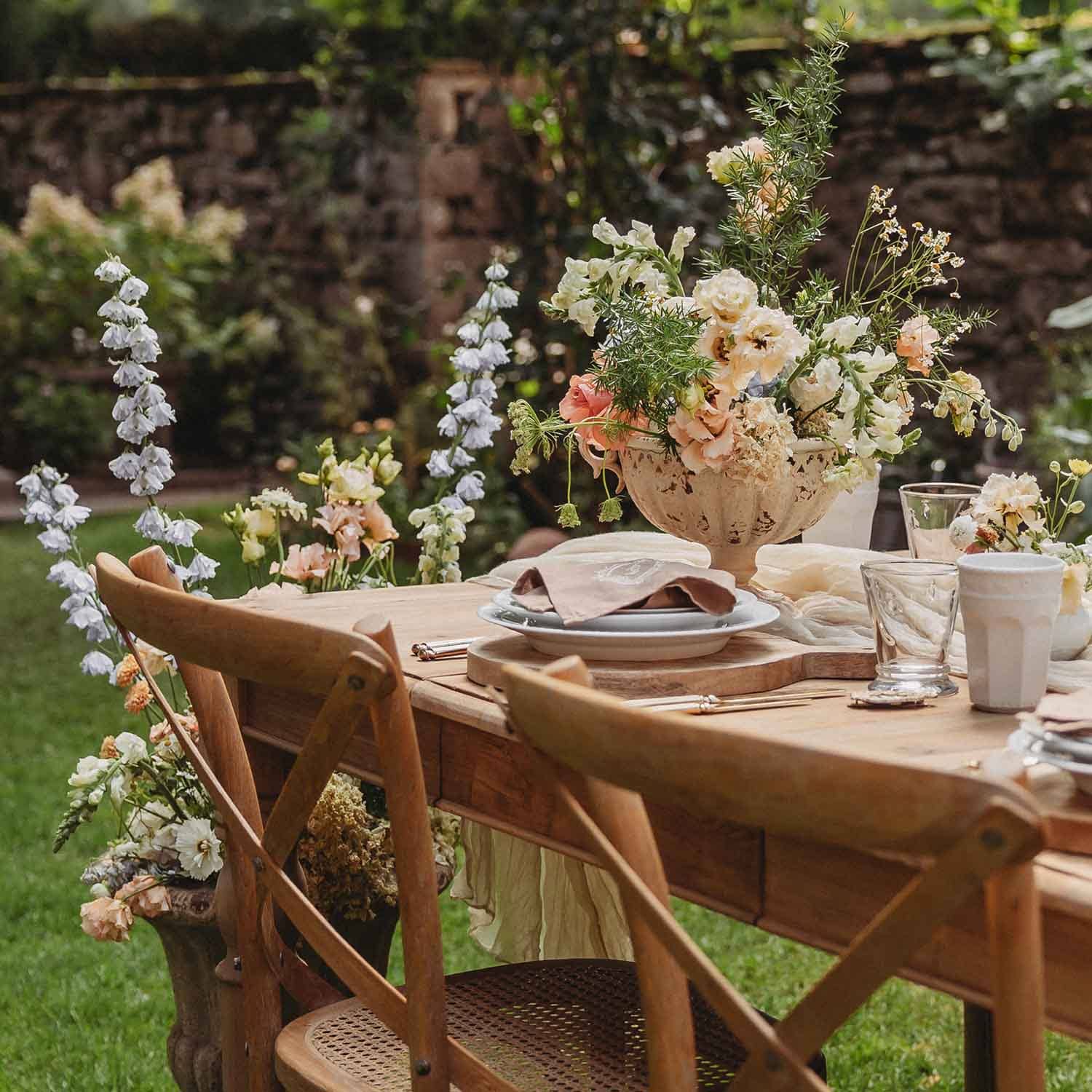 Houten tuintafel met rustieke stoelen en bloemendecoratie in pasteltinten