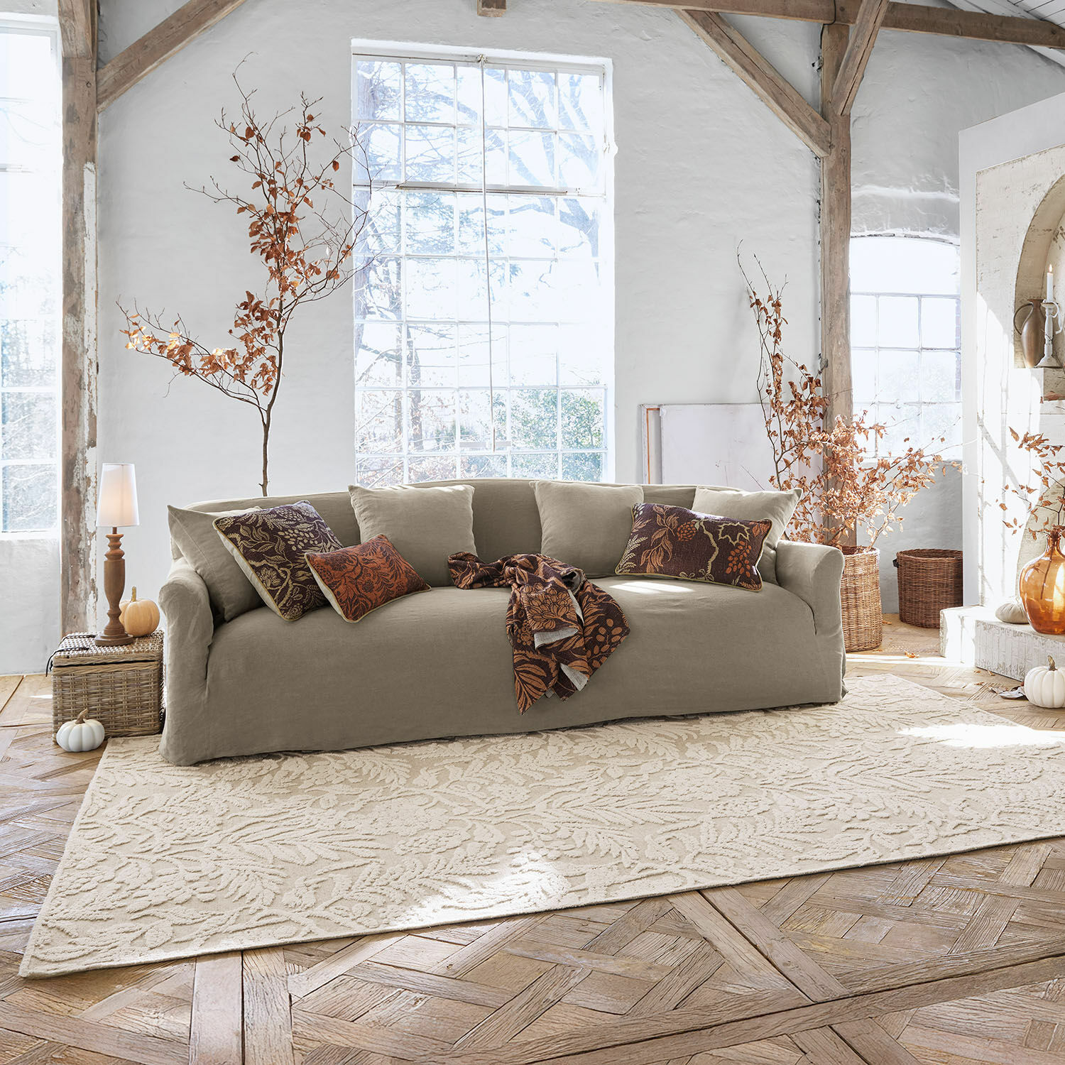 Vloerkleed Azimra Beige stoffen bank in lichte woonkamer met decoratieve kussens en vloerkleed met bladmotief