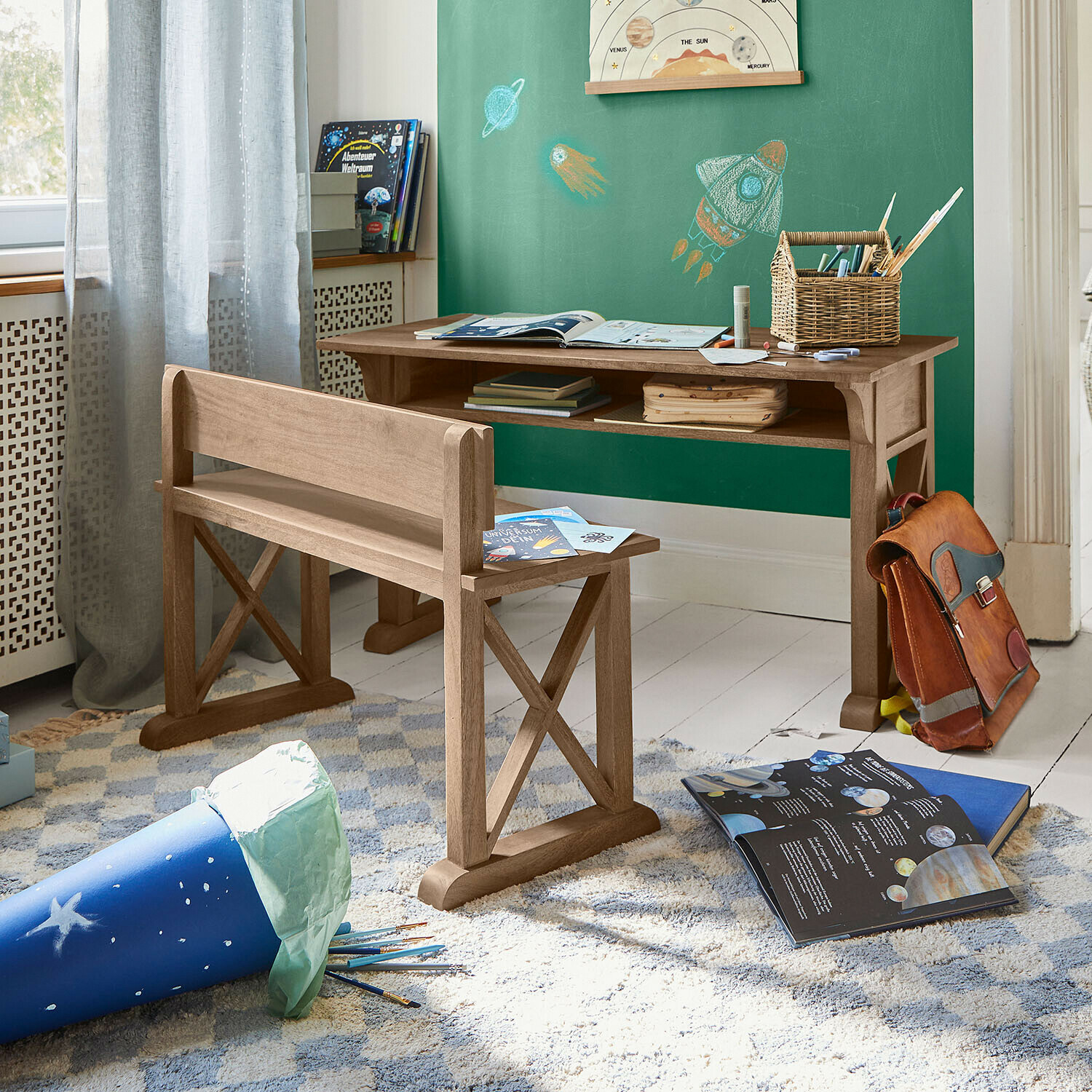 Kinderkamer met natuurlijk houten bureau en bankje, groene muur met ruimtevaartthema en open educatieve boeken