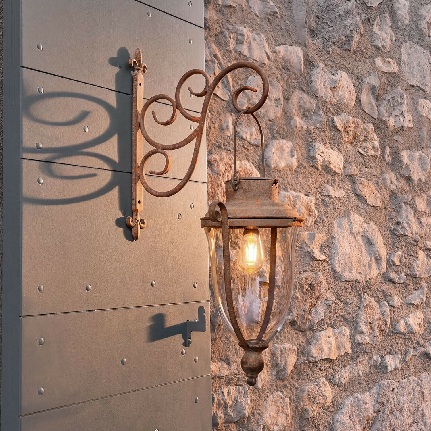 Rustieke buitenmuurlamp van metaal met roestkleur en helder glas gemonteerd op stenen muur