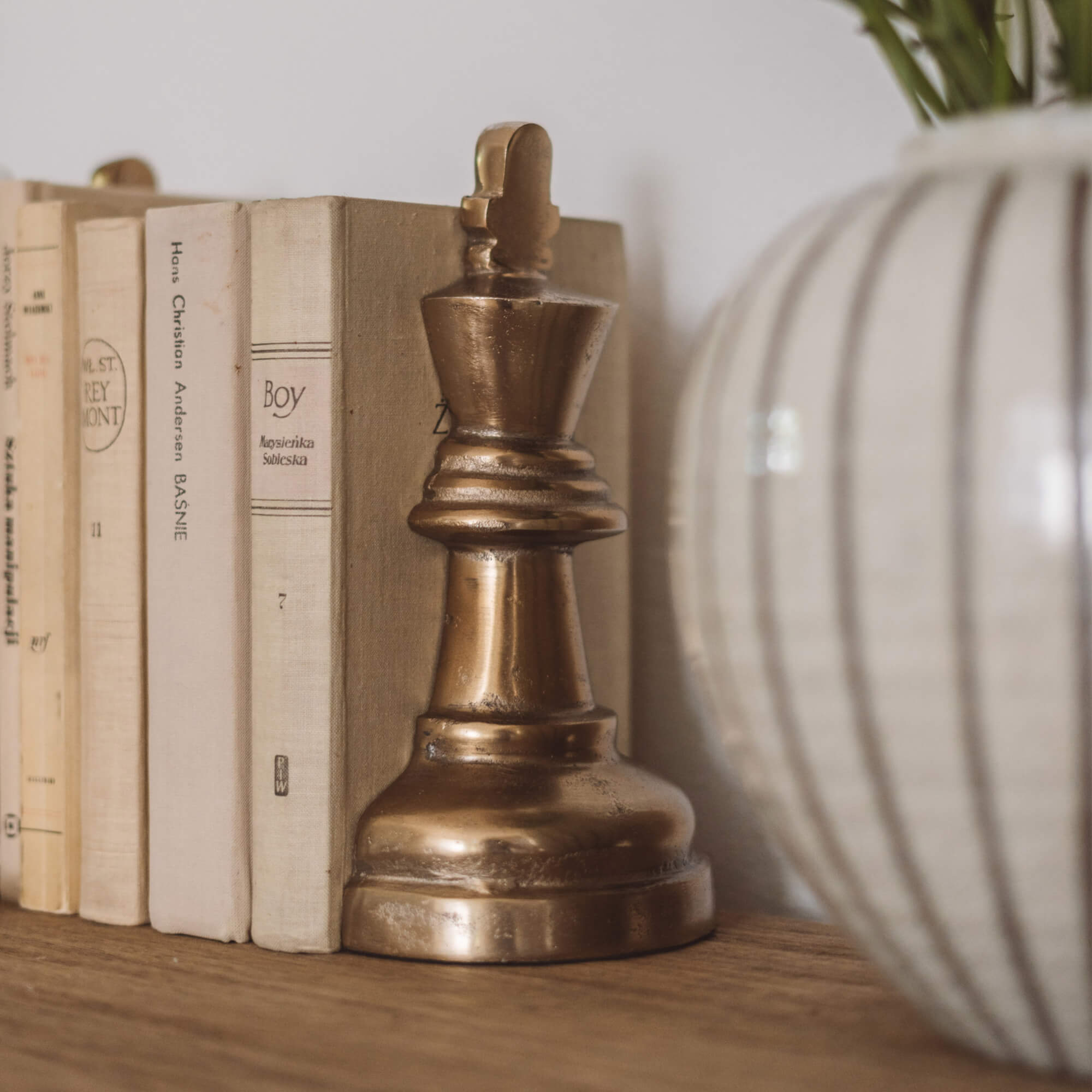 Gouden metalen schaakkoning beeldje op houten plank naast boeken en vaas