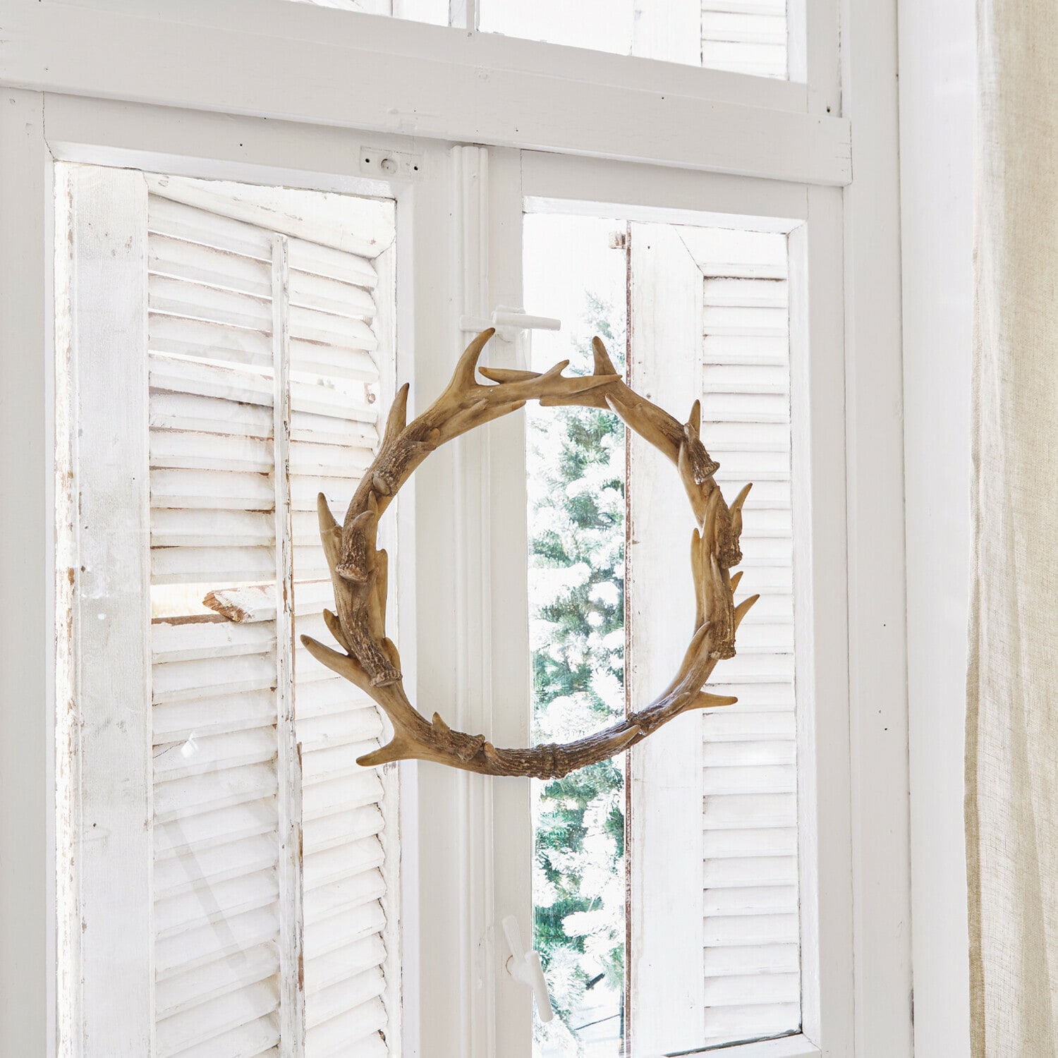 Krans Marcelle Decoratieve houten krans in geweivorm aan wit raam met kaarsen en dennenappels
