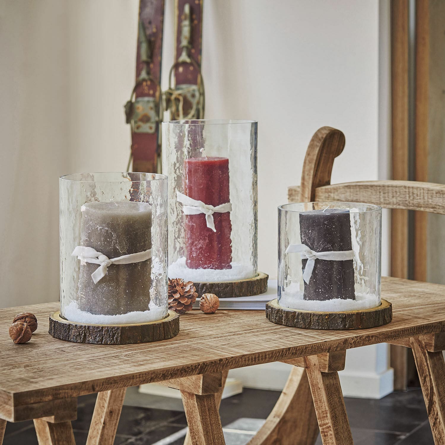 Drie glazen windlichten met houten voet en gekleurde kaarsen op houten tafel, sfeervolle interieurdecoratie
