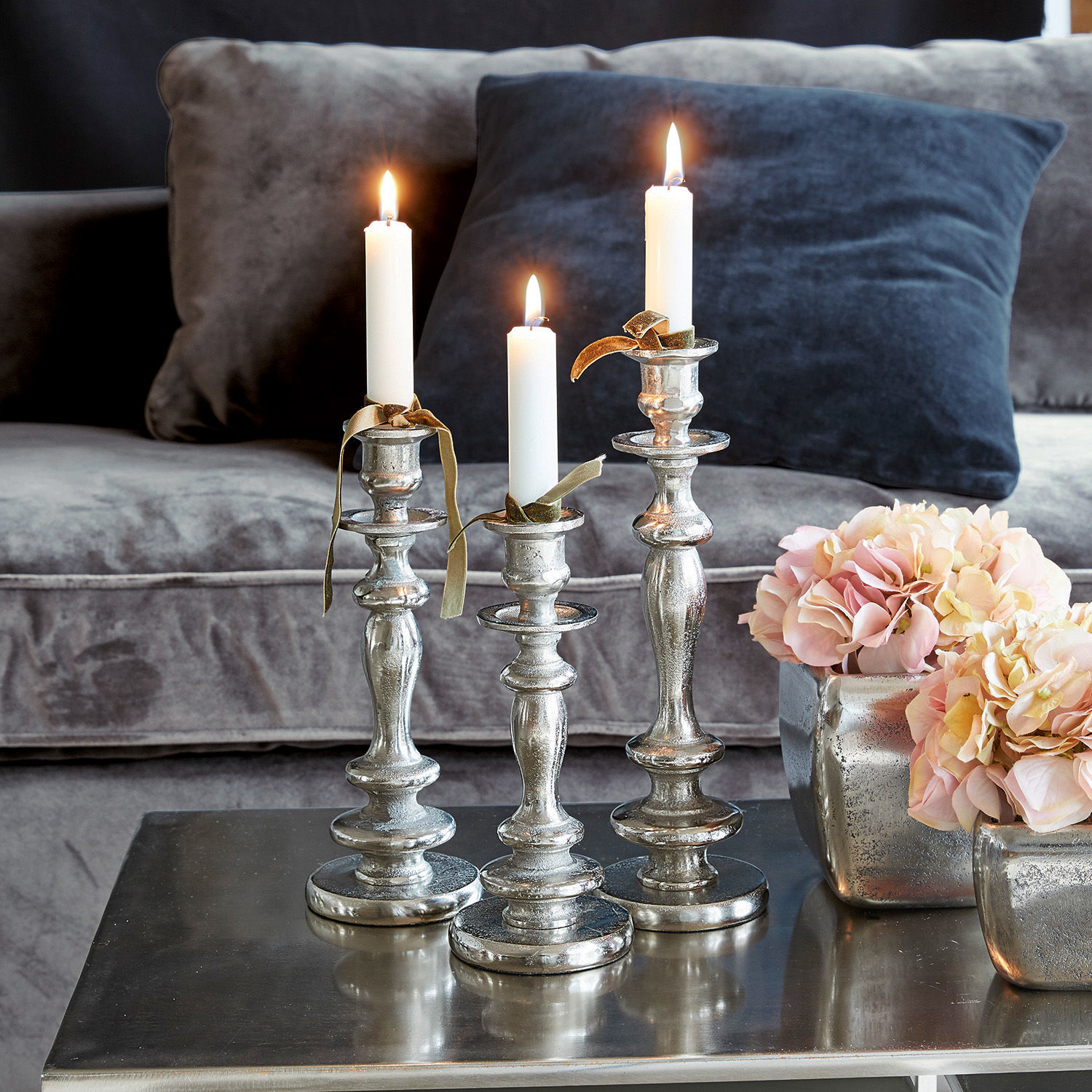 Set van drie zilverkleurige metalen kandelaars met witte kaarsen op een salontafel in de woonkamer