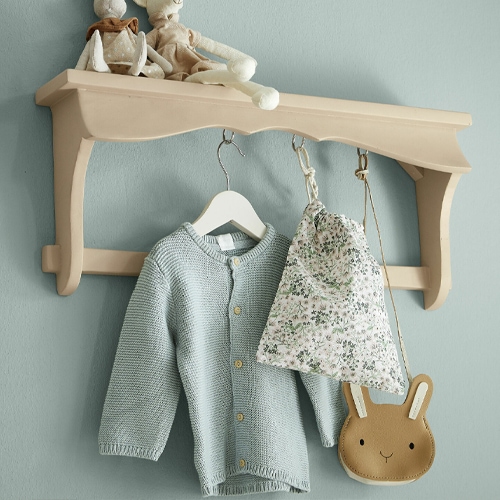 Beige houten wandplank met haken, met een lichtblauwe trui en een tas met bloemenpatroon