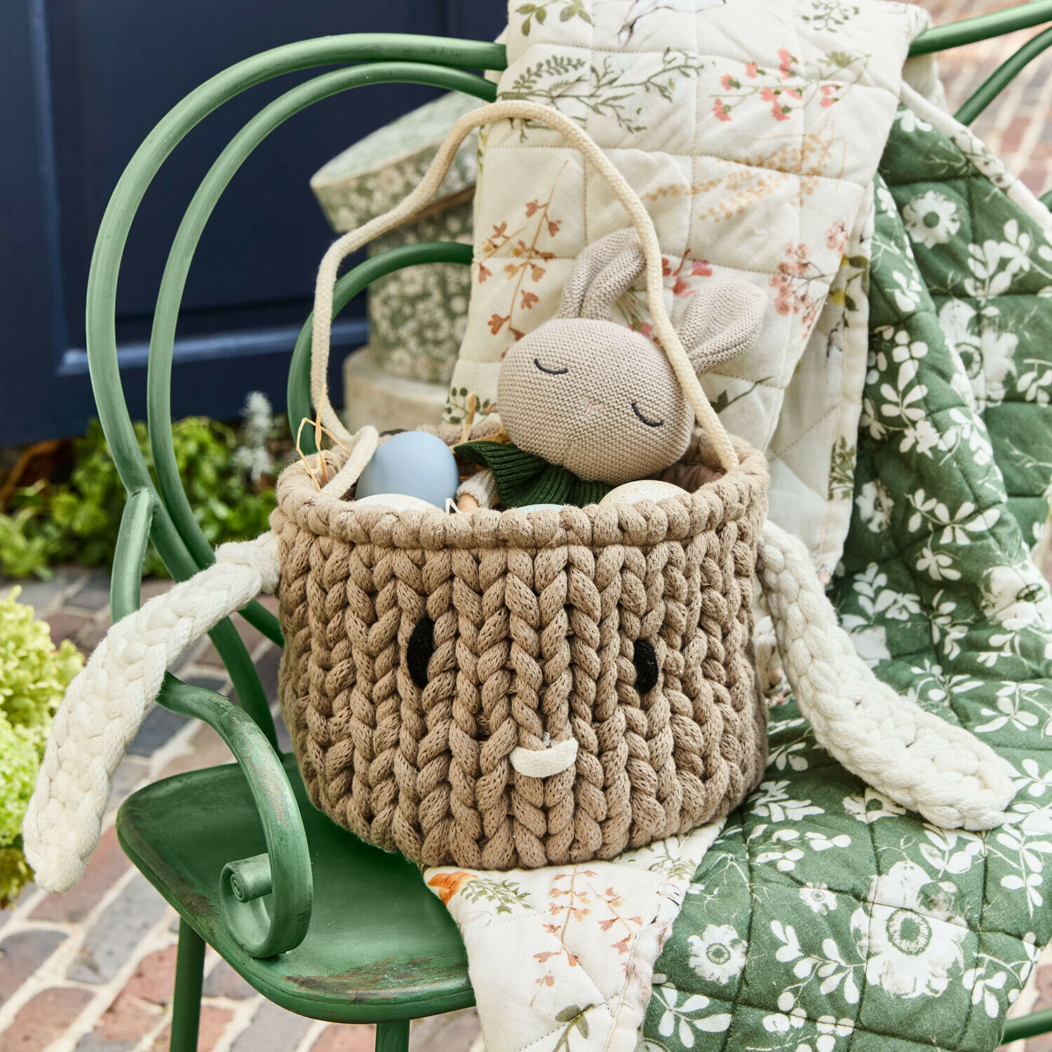 Bruine mand van gevlochten materiaal met oren en konijnenspeelgoed, paasdecoratie op groene stoel