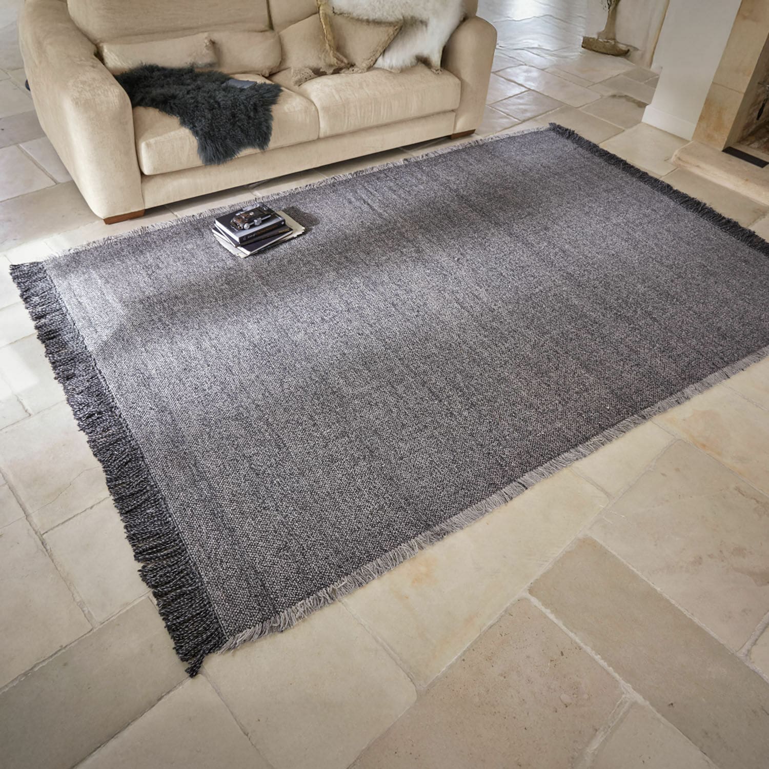 Vloerkleed voor binnen en buiten Marivela Grijs vloerkleed met franjes op lichte vloer in woonkamer met beige bank en sierkussens