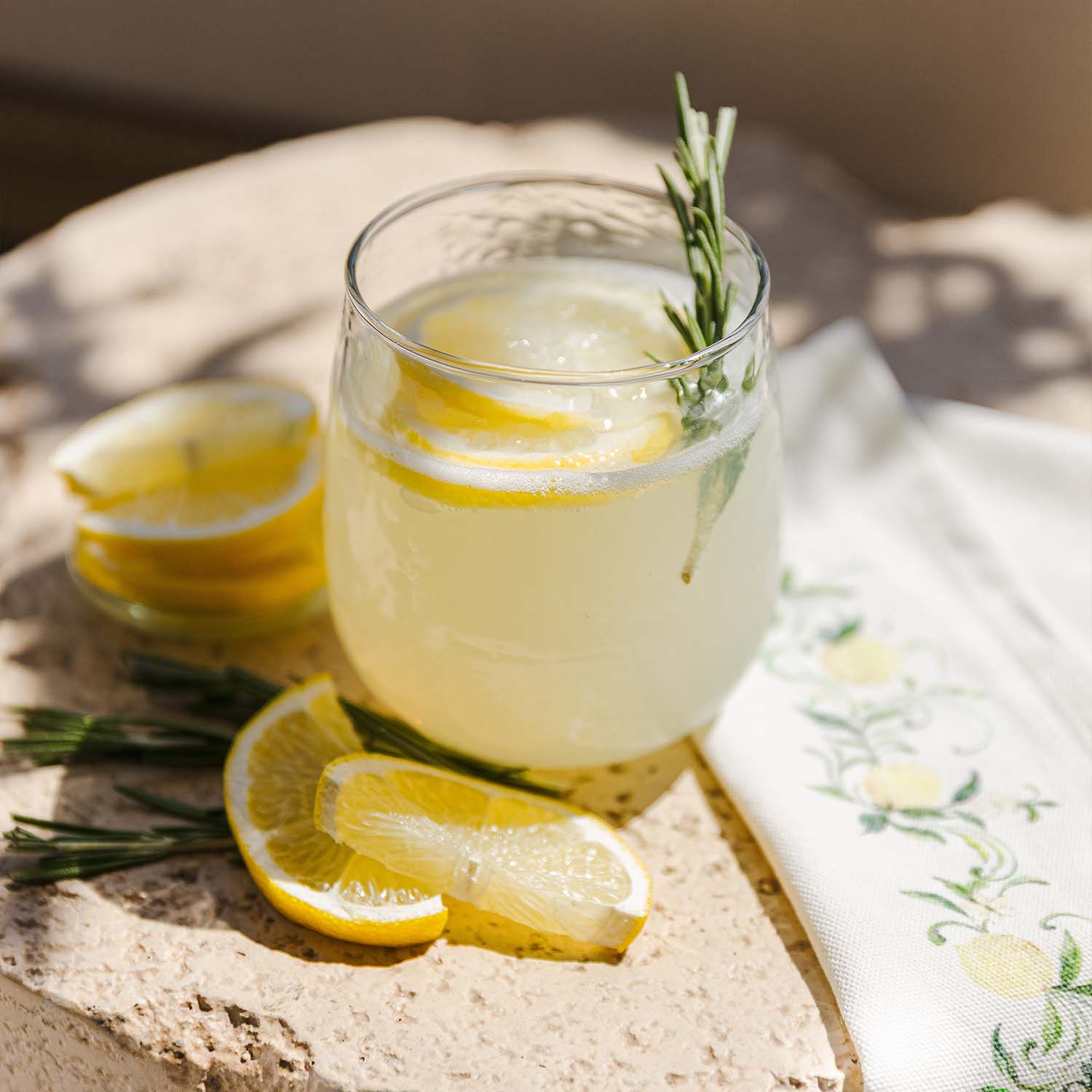 Glas limonade met citroenschijfjes en rozemarijn takje op stenen oppervlak met servet
