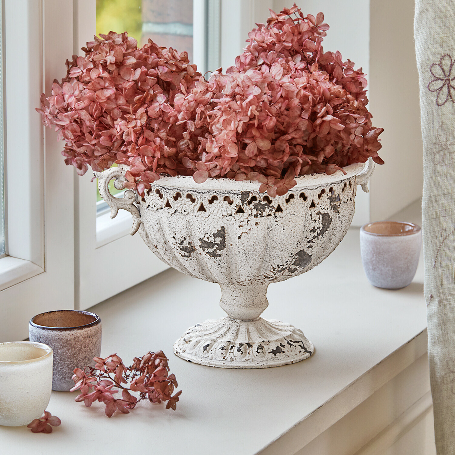 Witte metalen schaal met verweerde look en gedroogde roze bloemen op vensterbank