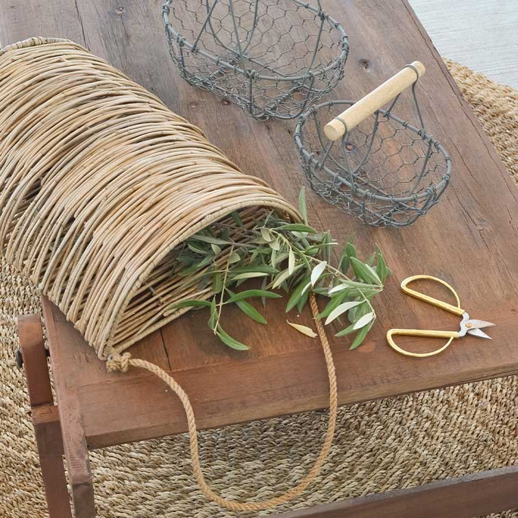 Rieten mand met touwhandvat op houten tafel met groene takken en gouden tuinschaar