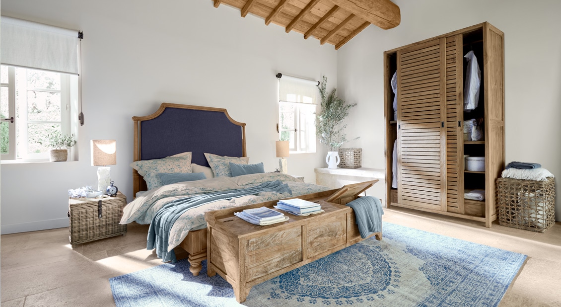 Slaapkamer met houten bed met blauw hoofdeinde, blauwe vloerkleed en natuurlijk houten meubels