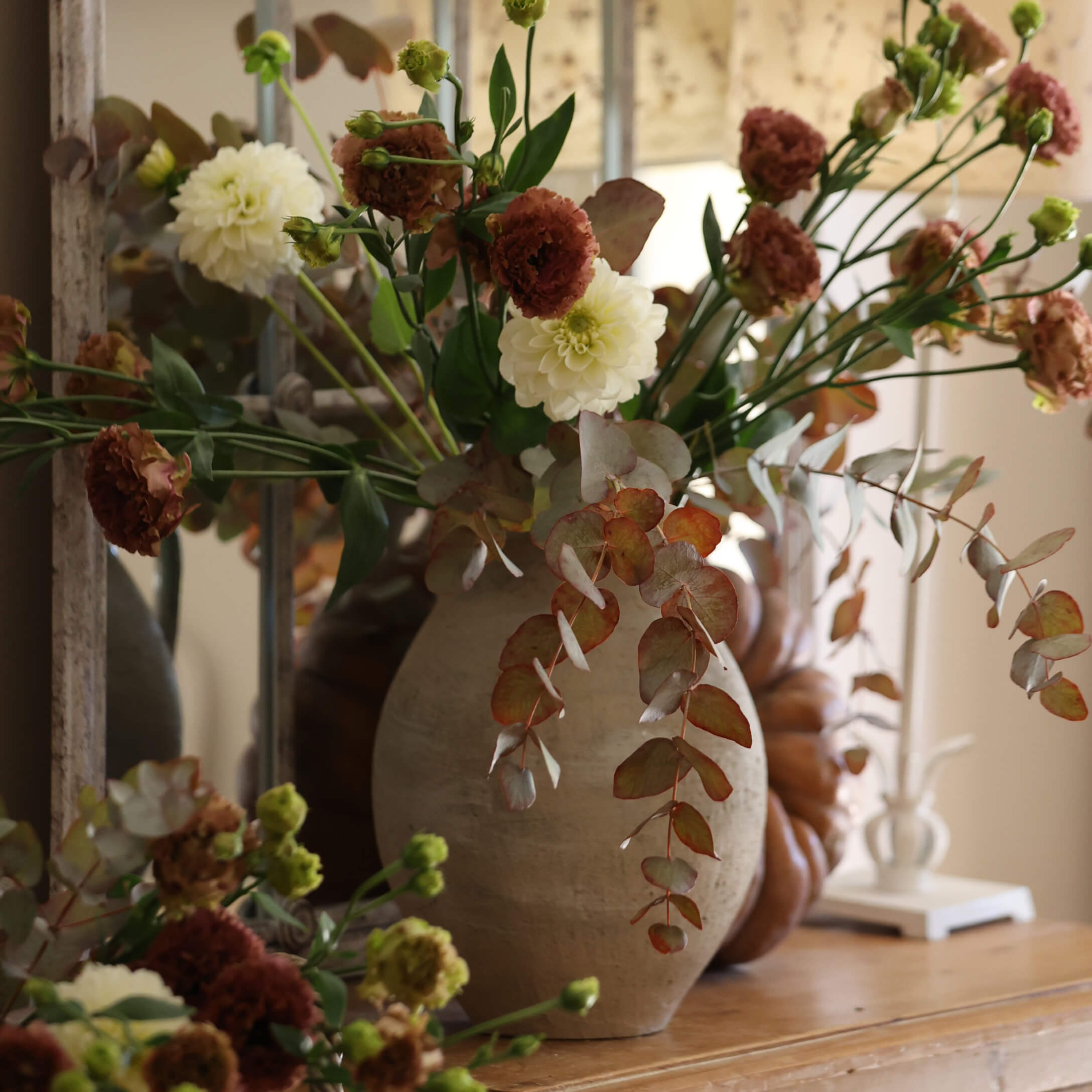 Beige keramische vaas met boeket witte en bruine bloemen op decoratieve houten tafel