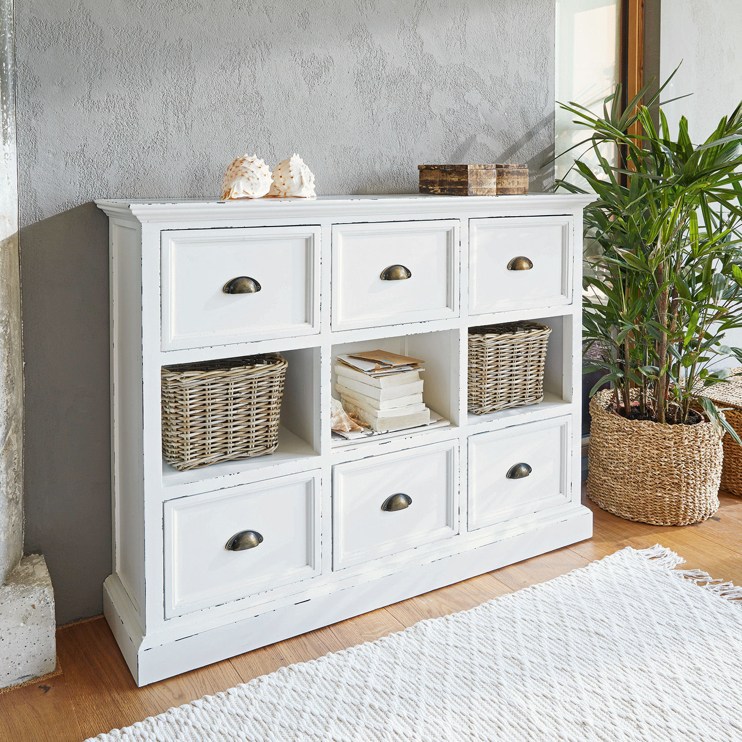 Witte houten ladekast met zes lades en drie open vakken, decoraties en plant ernaast