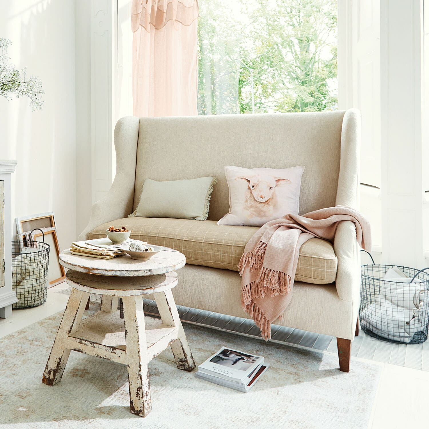 Beige stoffen bank met kussen met lammetjesmotief en rustieke houten salontafel in lichte kamer