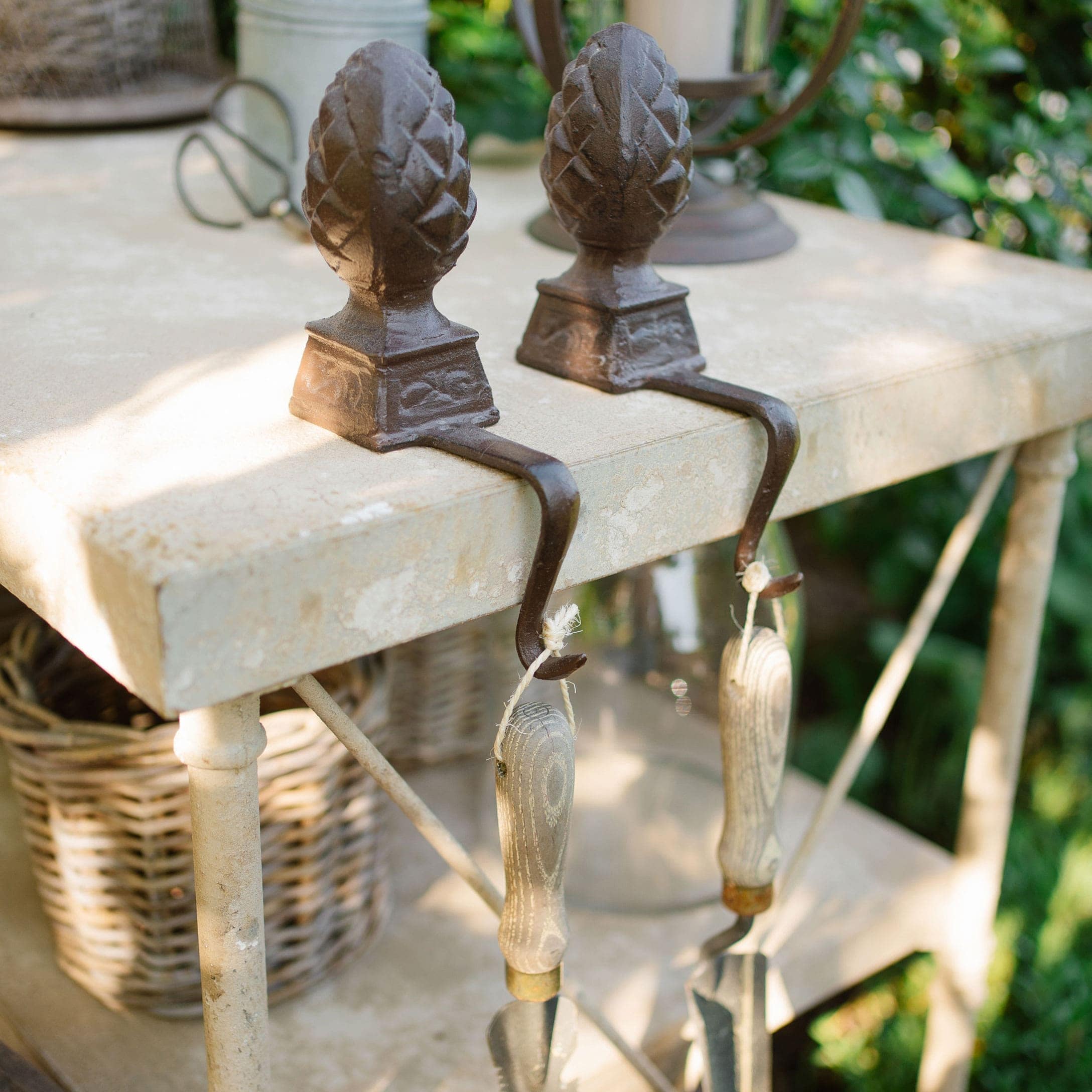 Set ijzeren haken met dennenappelmotief op beige tuintafel in zonlicht