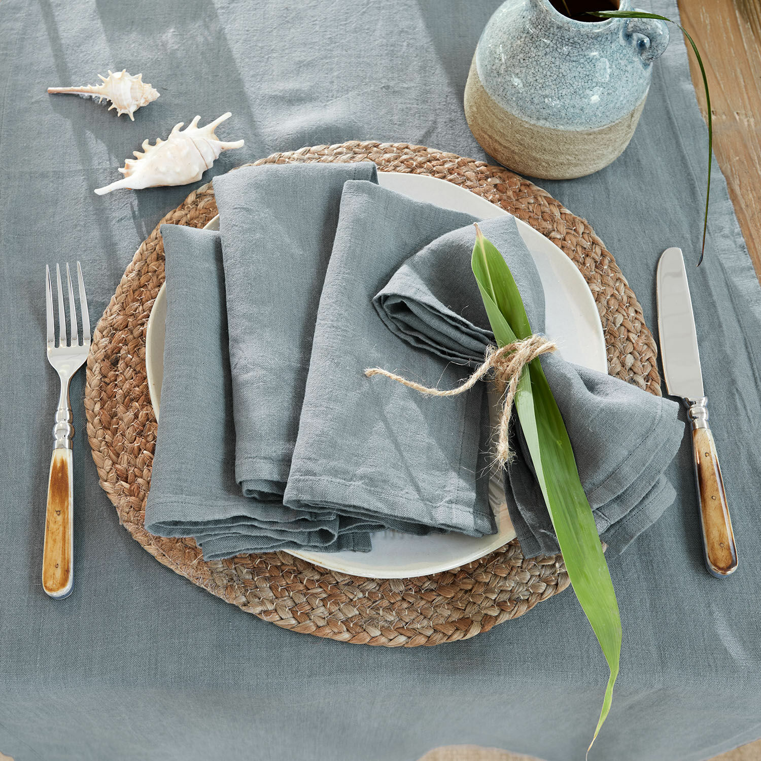 Grijze linnen tafelkleed en servetten op bord met natuurlijke onderzetter en bestek met houten handvat