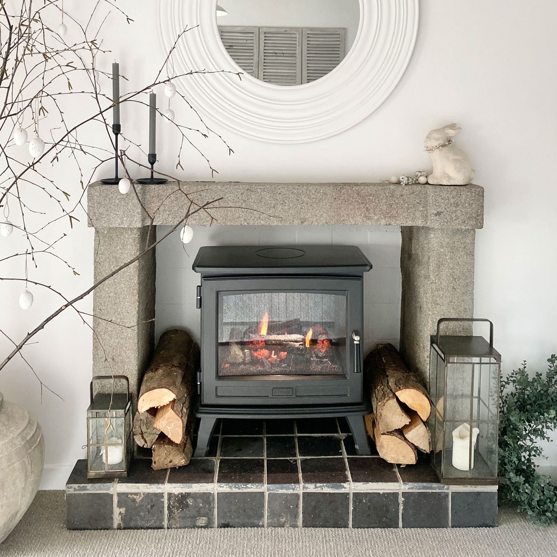 Zwarte houtkachel in stenen open haard met decoratieve houtblokken en rustieke lantaarns