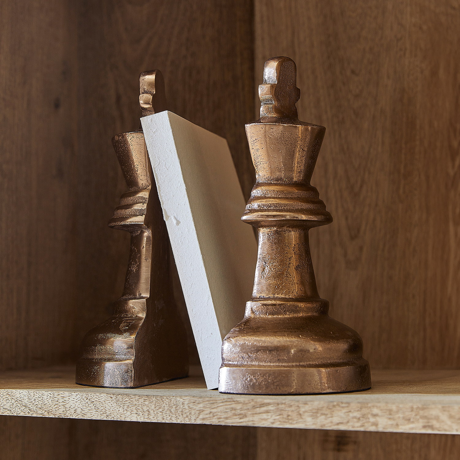 Boekensteunen in de vorm van schaakstukken in koperen kleur op houten plank
