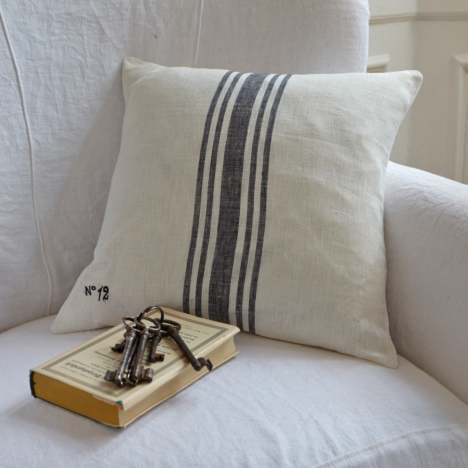 Decoratief linnen kussen in crème met zwarte strepen op witte bank met boek en sleutels