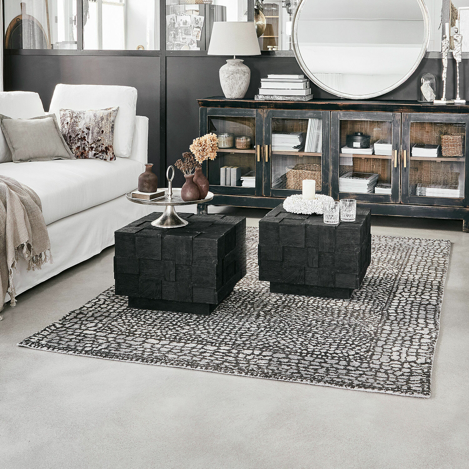 Moderne woonkamer met witte bank en zwarte houten salontafels op een patroon vloerkleed