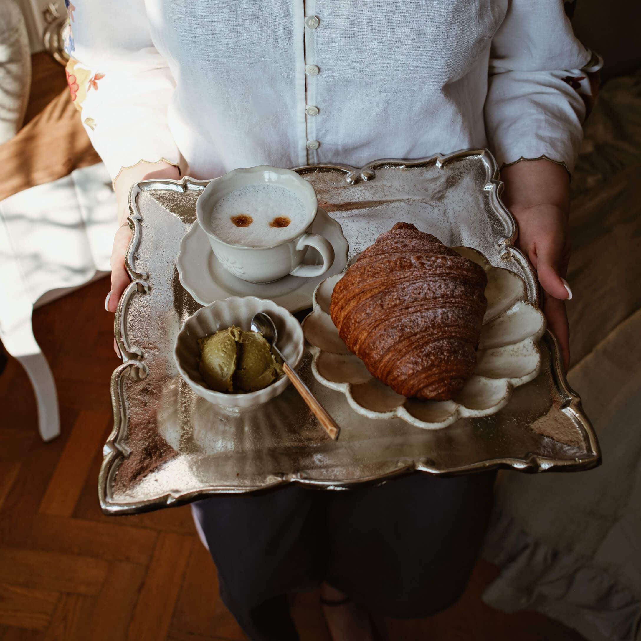 Metalen dienblad met croissant, kop koffie en groene boter op wit porselein