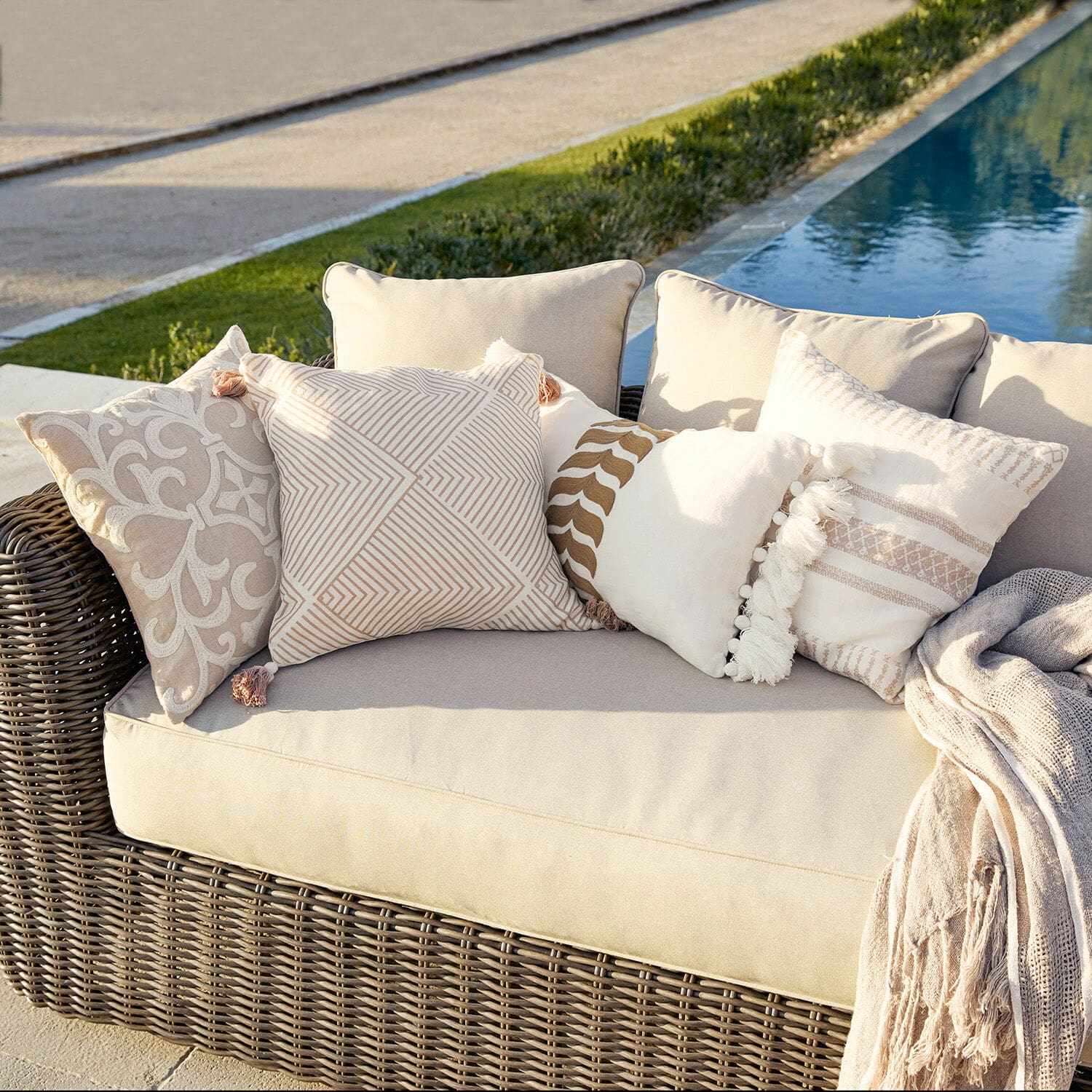 Kussenhoes set van 4 Olette Beige rotan bank met crèmekleurige en beige sierkussens buiten bij het zwembad