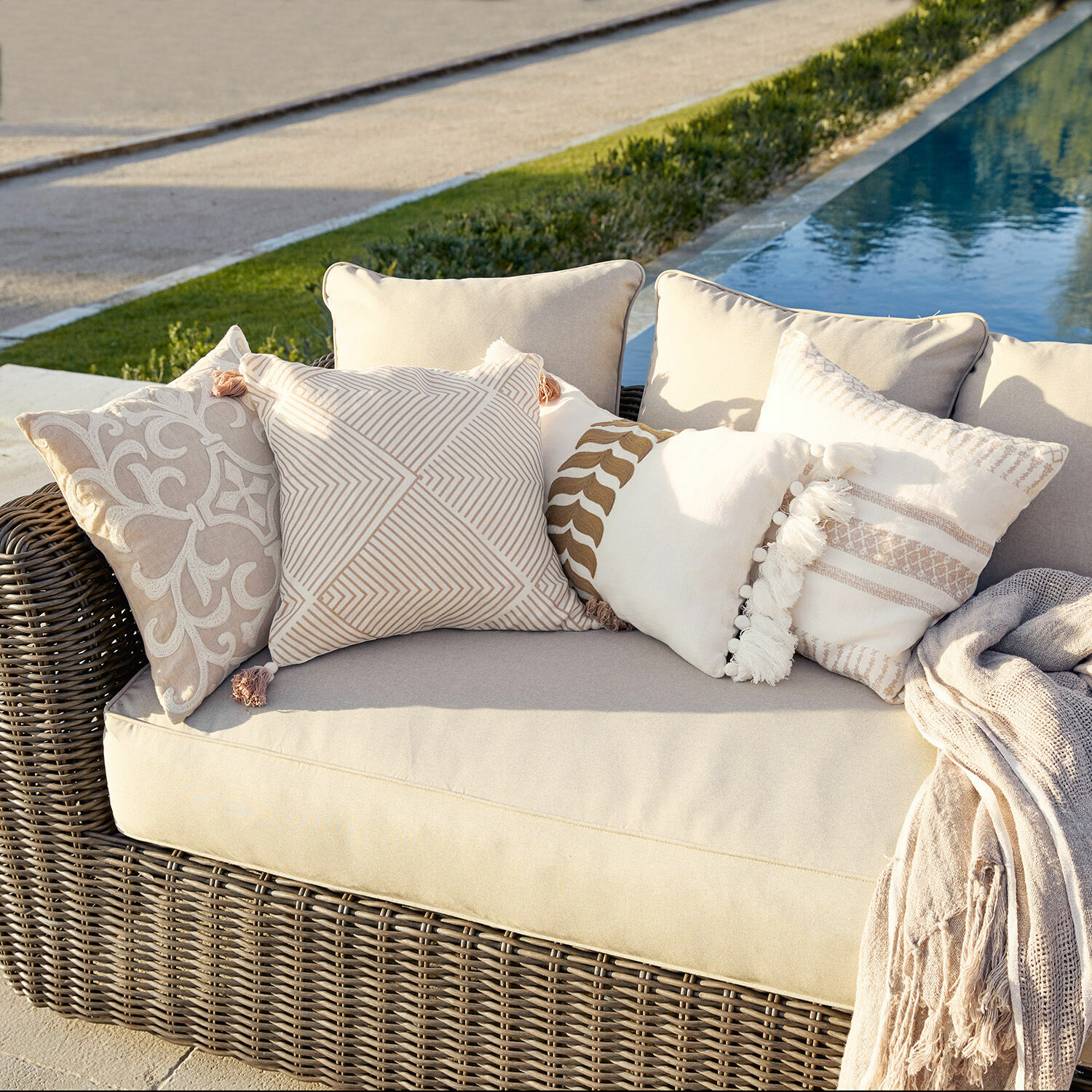 Kussenhoes set van 4 Olette Beige rotan bank met crèmekleurige en beige sierkussens buiten bij het zwembad