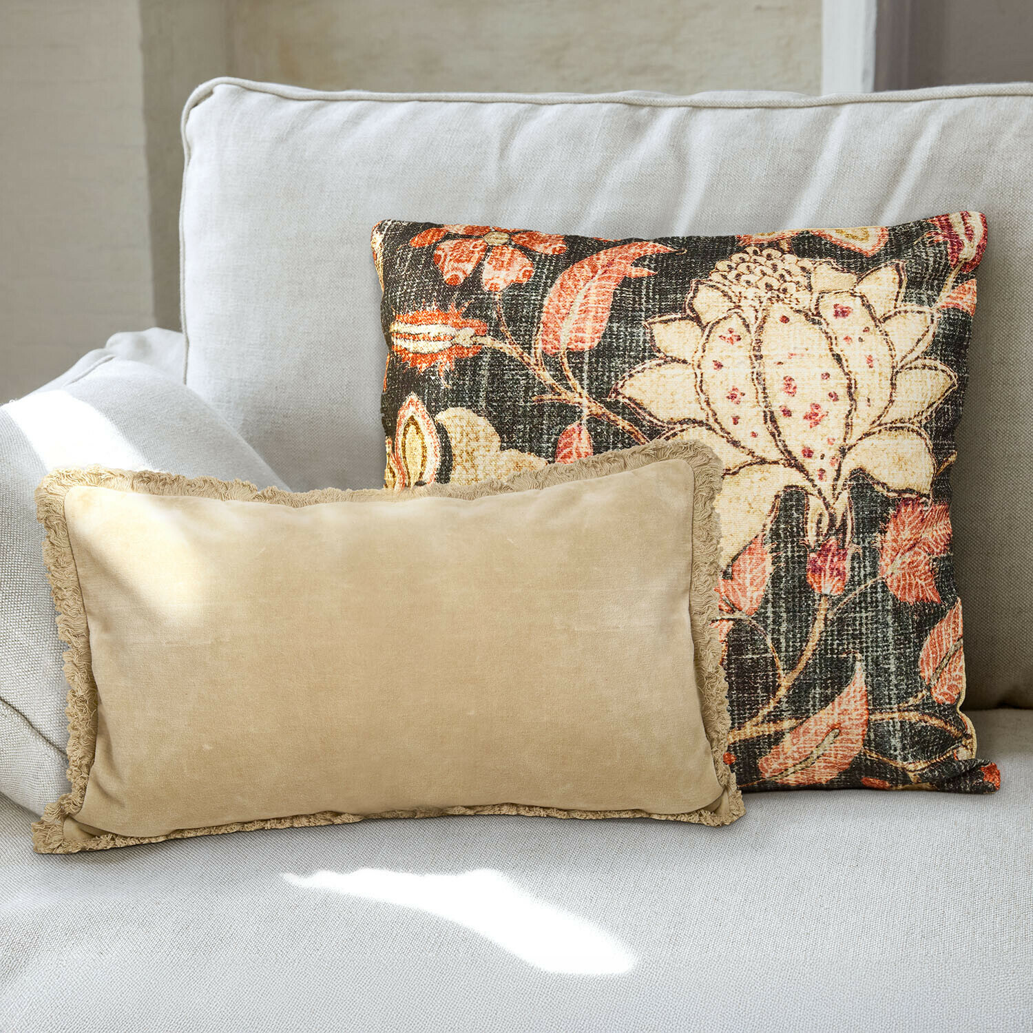 Kussenhoes set van 2 Ambrayelle Twee decoratieve kussens op een lichtgrijze bank, één beige met franjes, de ander met kleurrijk bloemenpatroon